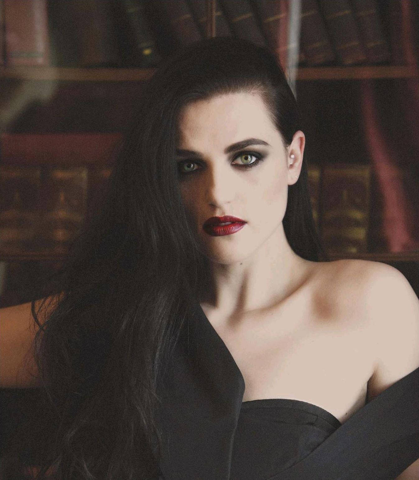 Katie 桌布 壁紙 — 一位深色頭髮、大膽紅唇的女性，在一個光線昏暗、裝滿皮革裝訂書籍的圖書館中凝視著。