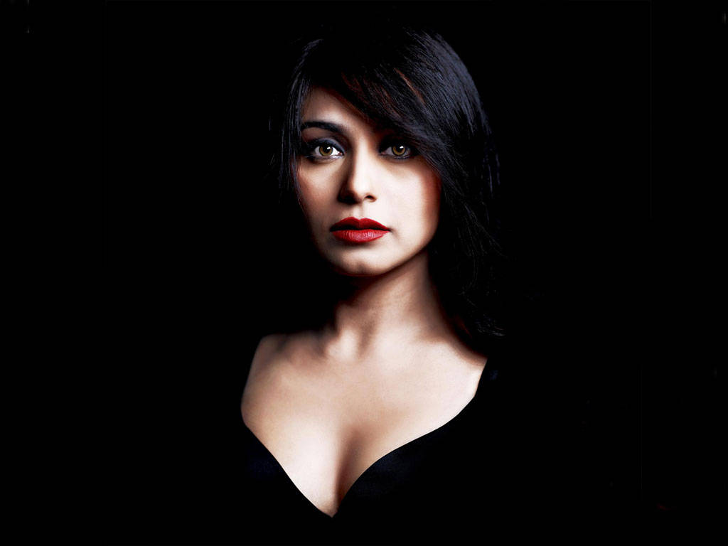 Rani Mukerji 桌布 壁紙 — 一位深色頭髮、大膽紅唇的女性在純黑背景下強烈凝視。
