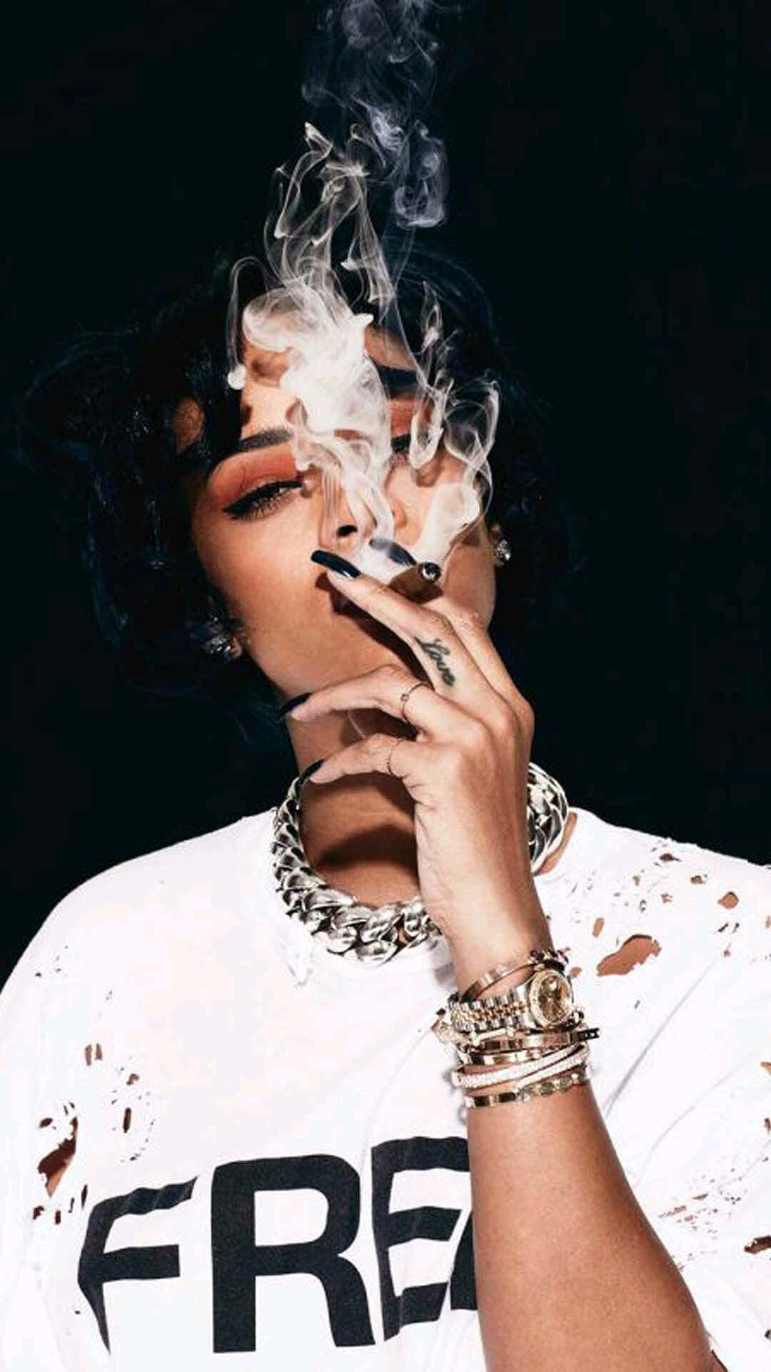cigar 桌布 壁紙 — 一位深色頭髮、妝容大膽的女性，在黑色背景下吸煙並呼出煙霧。