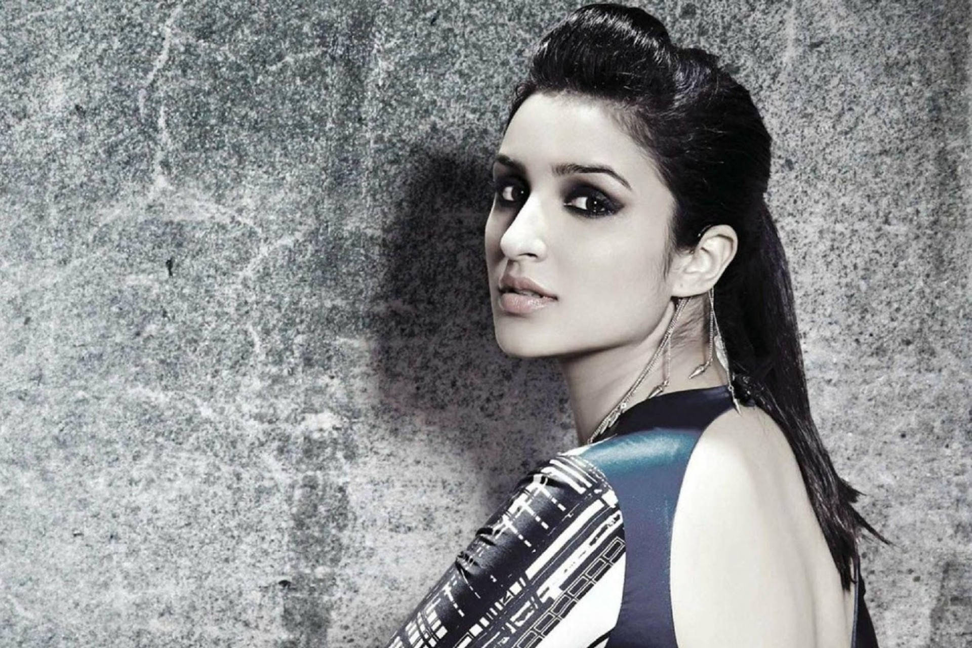 Parineeti 桌布 壁紙 — 一位深色頭髮、妝容大膽的女性，穿著時尚的無袖上衣，靠在一面有紋理的灰色混凝土牆上。