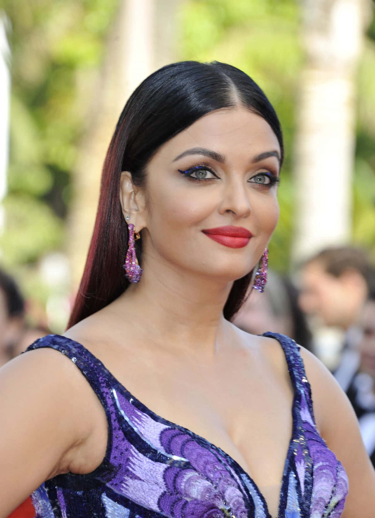Aishwarya Rai 桌布 壁紙 — 一位深色頭髮、妝容大膽的女性，身穿閃亮紫色連衣裙和相配的耳環，微笑著。