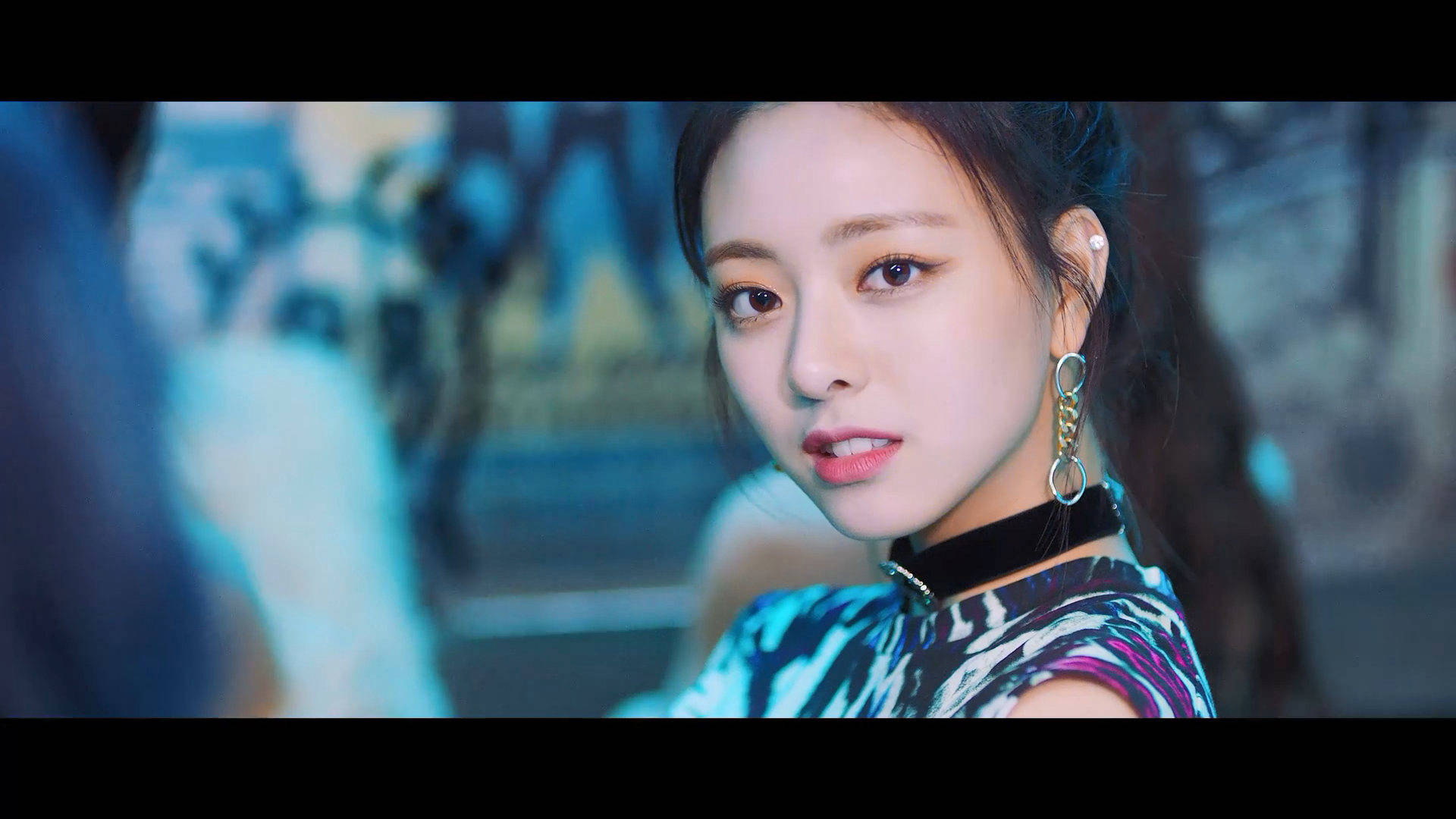 ITZY 桌布 壁紙 — 一位深色頭髮、妝容大膽的年輕女性在冷藍色燈光下直視鏡頭，身穿圖案上衣和大圈耳環。
