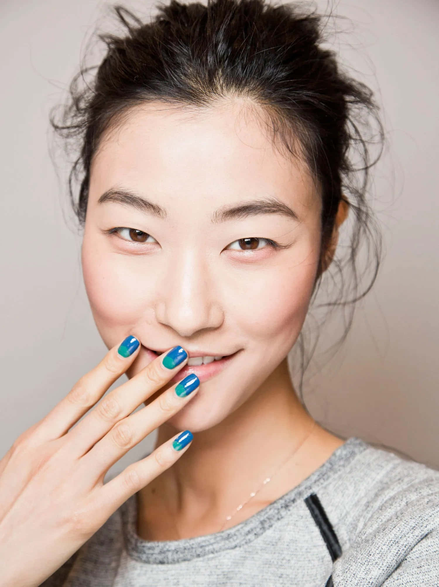 Spring Makeup 桌布 壁紙 — 一位深色頭髮、帶有鮮豔藍綠色指甲的微笑女士，輕輕用手遮住嘴巴。