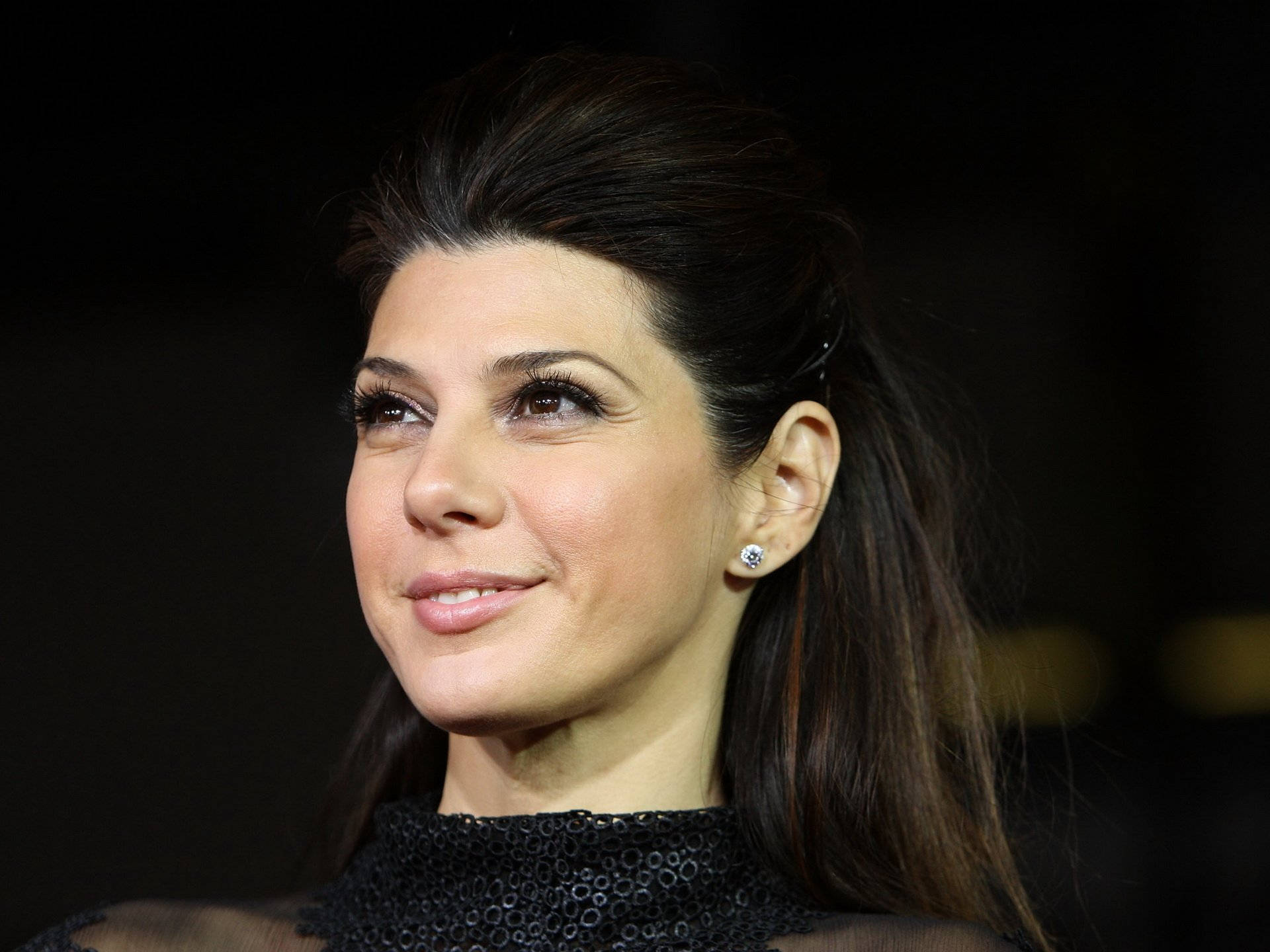 Marisa Tomei 桌布 壁紙 — 一位深色頭髮、帶著微妙微笑的女性特寫肖像，身穿黑色亮片上衣，戴著鑽石耳釘。