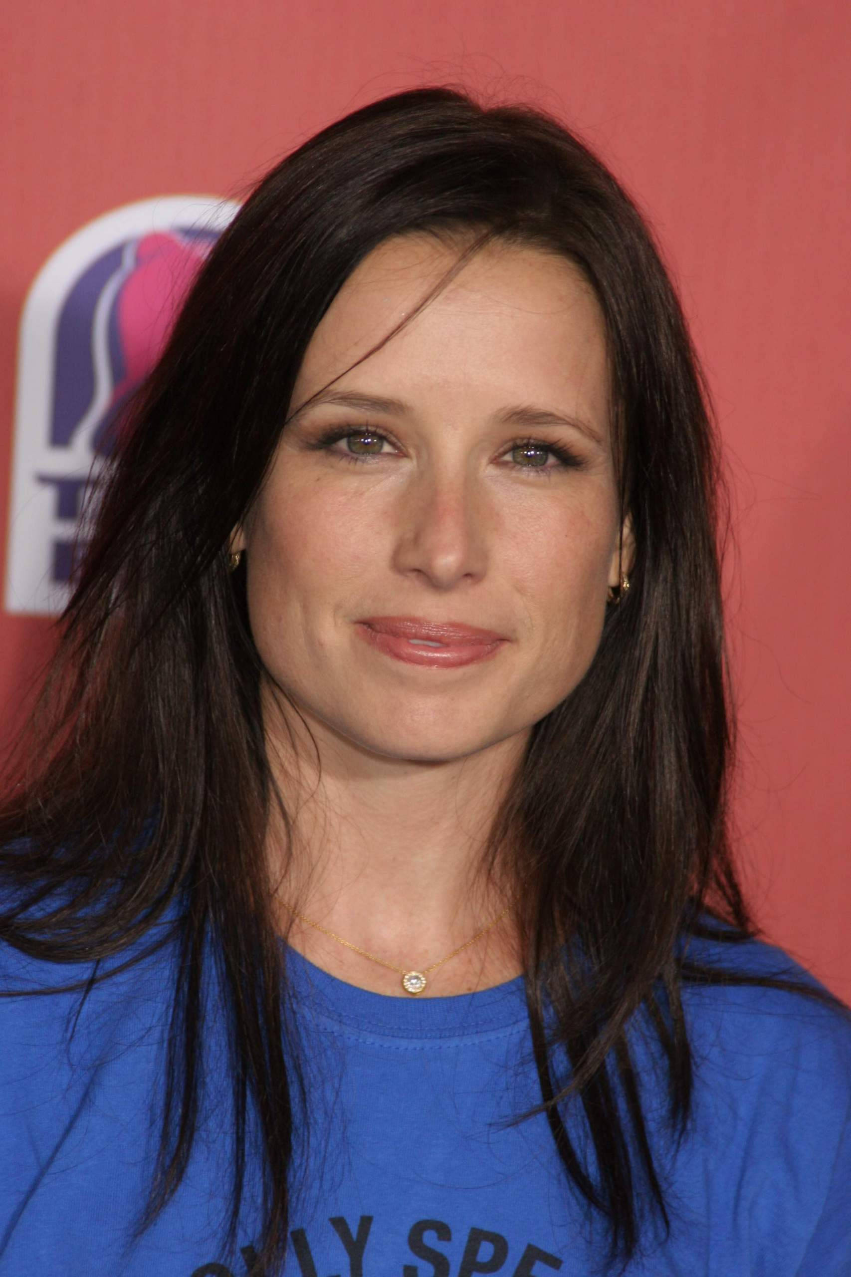 Celebrity 桌布 壁紙 — 一位深色頭髮、帶著溫柔微笑的女性，在帶有標誌的紅色背景前穿著藍色T恤。