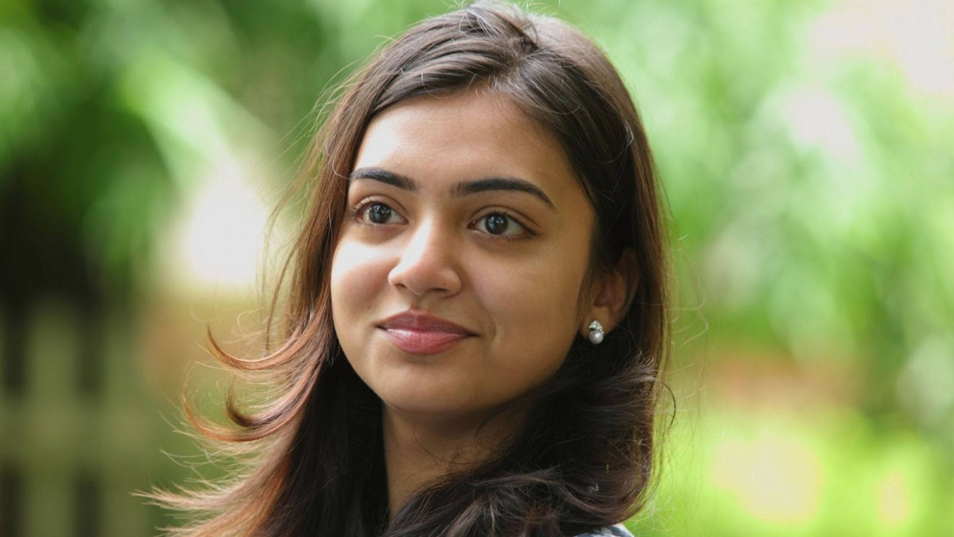 Indian 桌布 壁紙 — 一位深色頭髮、帶著溫柔微笑的年輕女性，在柔和的綠色模糊背景前看向鏡頭。