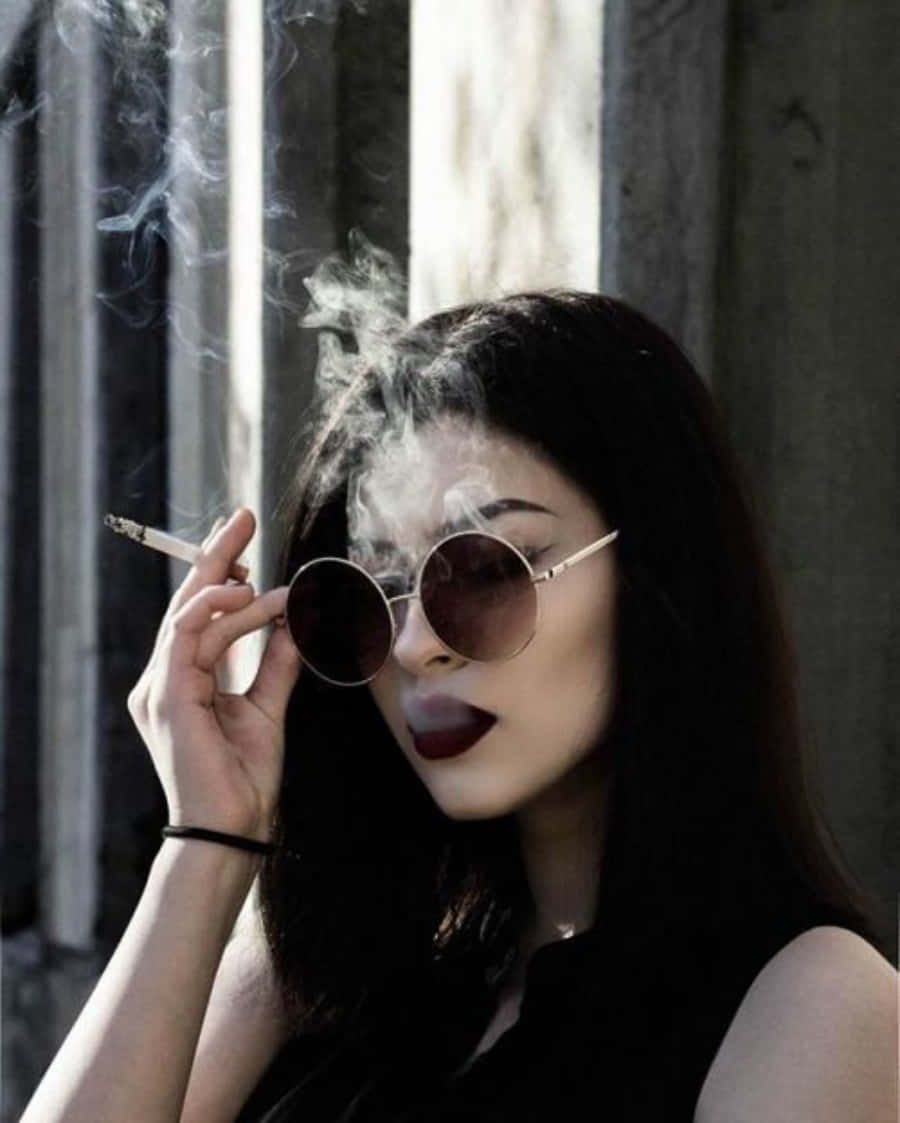 抽菸 桌布 壁紙 — 一位深色頭髮、戴圓形太陽眼鏡的女性，在陽光透過垂直柵欄照射的窗邊抽煙。