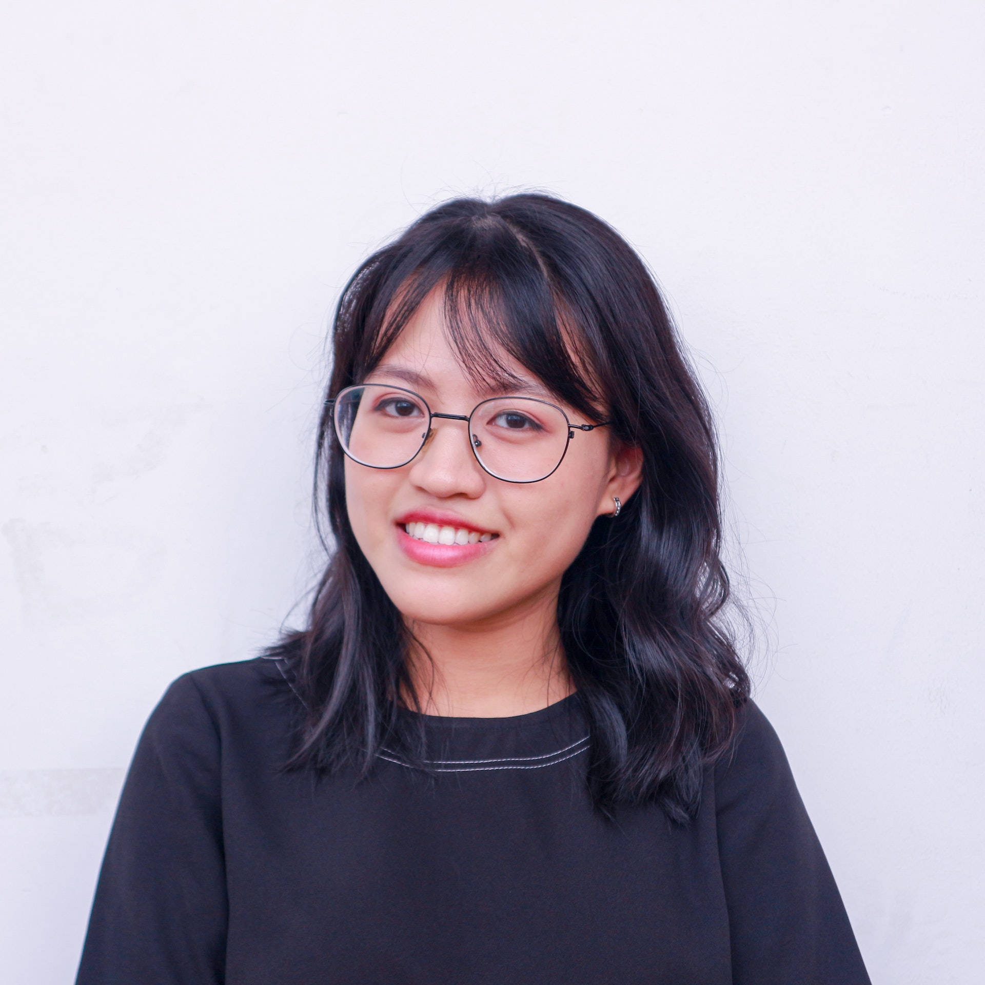 smiling 桌布 壁紙 — 一位深色頭髮、戴眼鏡的年輕女性，在白色牆壁前溫暖地微笑。