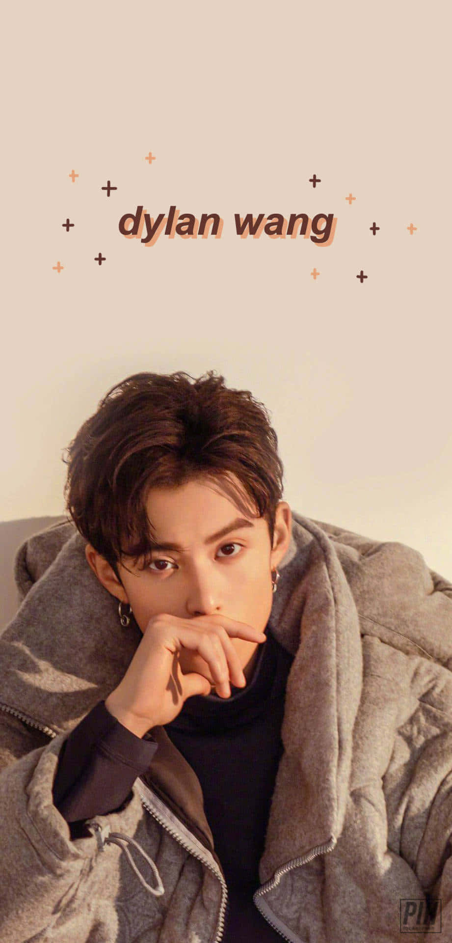 Dylan Wang 桌布 壁紙 — 一位深色頭髮、戴耳環的年輕男子，身穿灰色羽絨外套，手托下巴，靠在柔和的米色背景上，背景有「dylan wang」文字和星形裝飾。