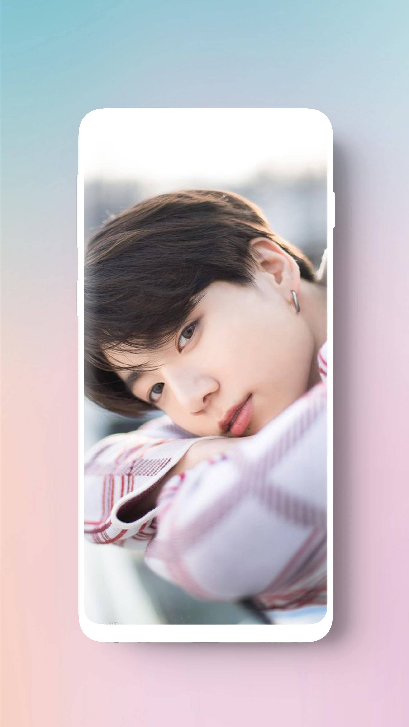 BTS 桌布 壁紙 — 一位深色頭髮、戴耳環的年輕男子，穿著格紋襯衫，將頭靠在手臂上，背景是柔和的漸層色。