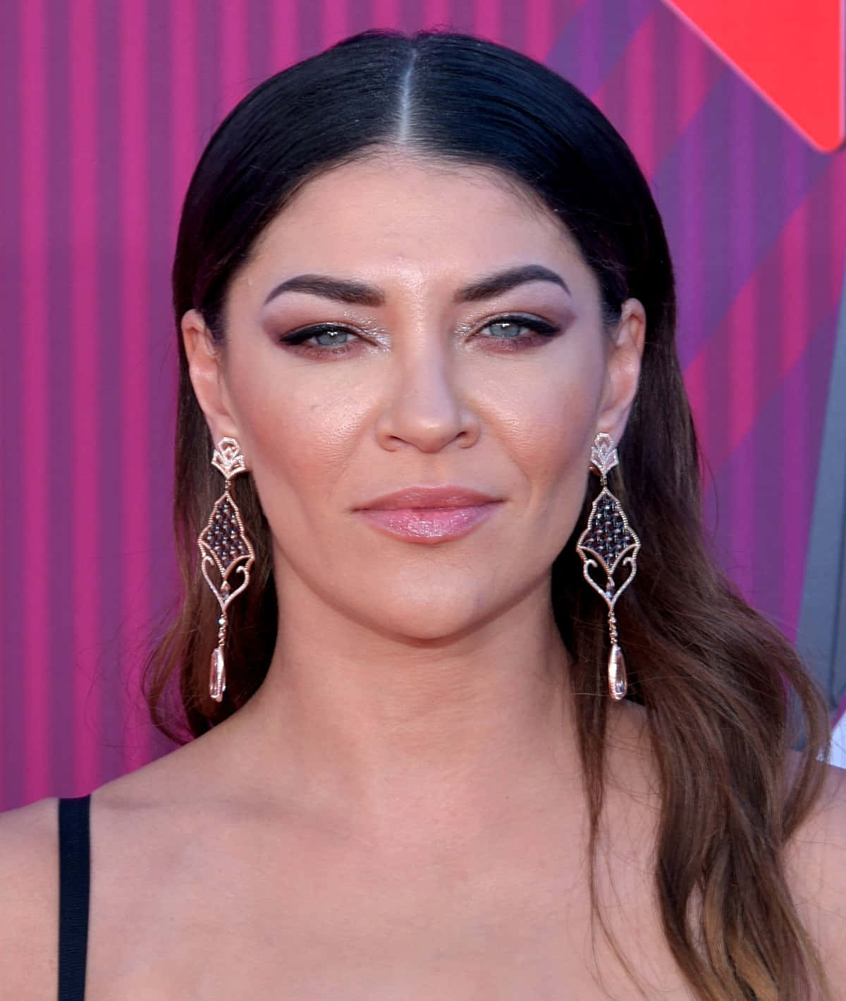 jessica szohr 桌布 壁紙 — 一位深色頭髮、戴著優雅垂墜耳環的女性，在充滿活力的粉紅條紋背景前擺姿勢。
