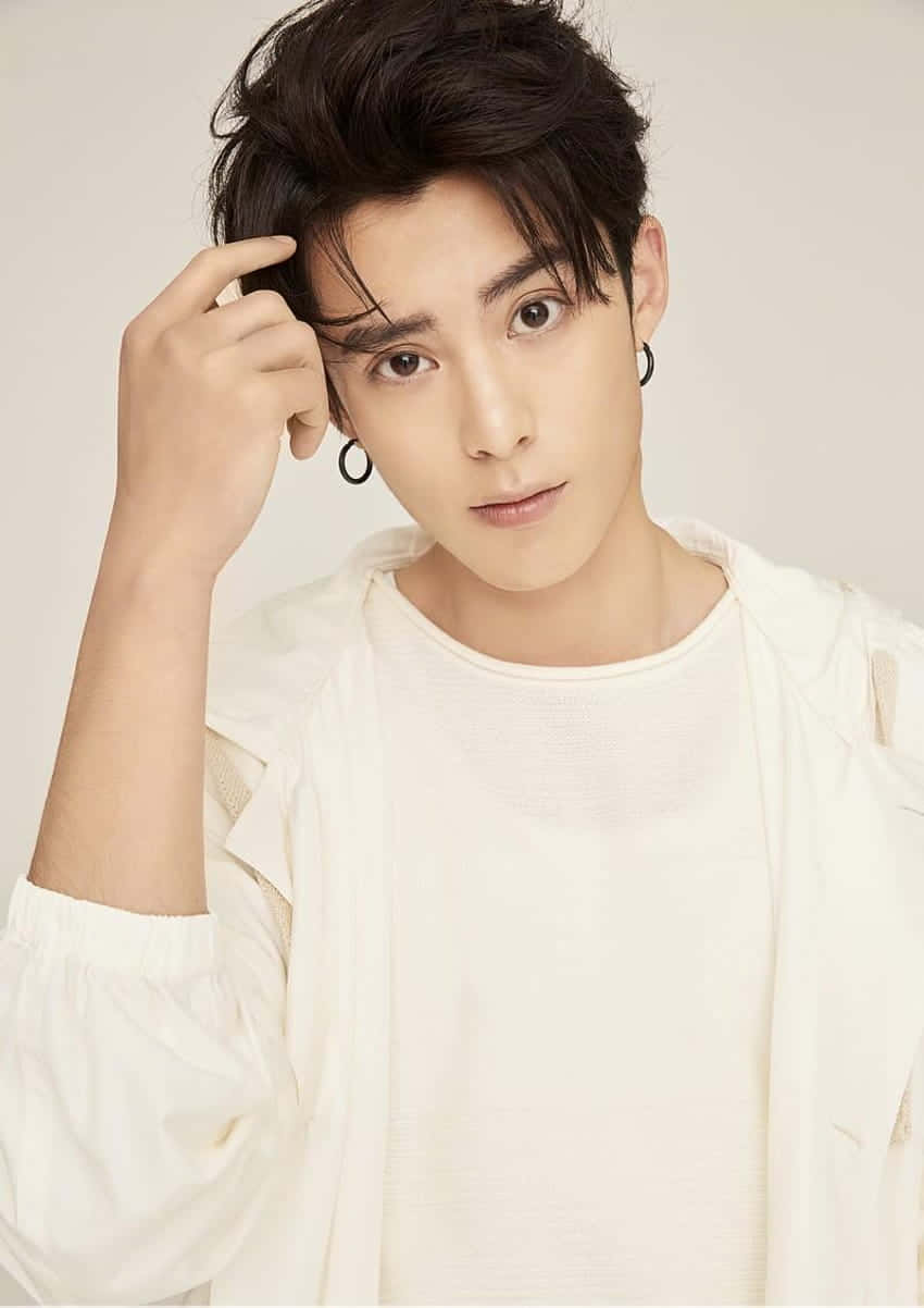 Dylan Wang 桌布 壁紙 — 一位深色頭髮、戴著圈形耳環的年輕男子，在純色背景前穿著白色紋理上衣，輕輕觸碰太陽穴。