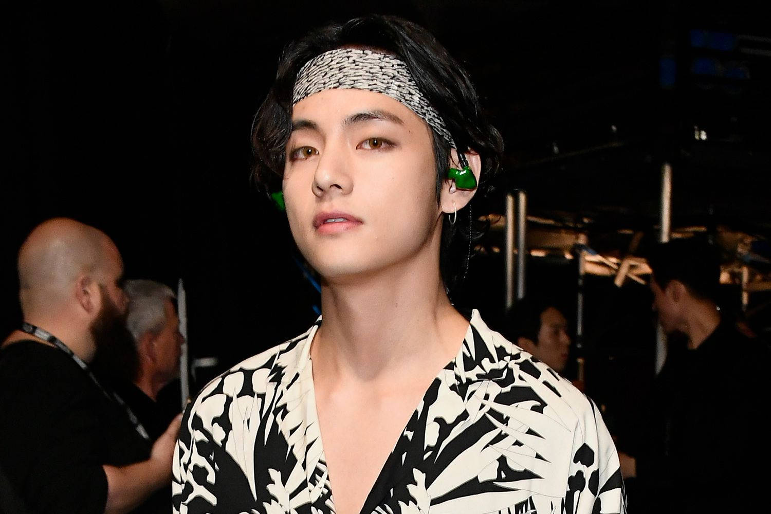BTS 桌布 壁紙 — 一位深色頭髮、戴著圖案頭帶的年輕男子，在舞台燈光下穿著大膽的黑白花卉襯衫。