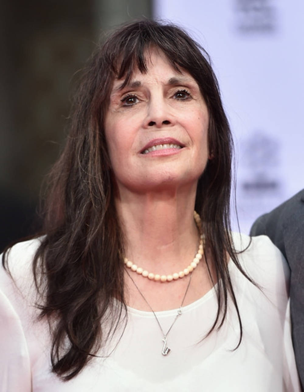 Celebrity 桌布 壁紙 — 一位深色頭髮、戴著珍珠項鍊的女性在活動中向上看，溫柔地微笑。