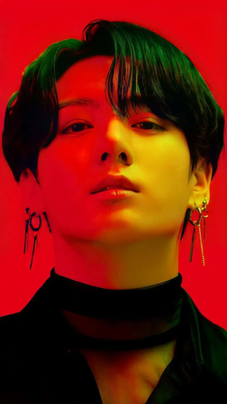 Jungkook 桌布 壁紙 — 一位深色頭髮、戴著耳環的人，在鮮紅色背景與戲劇性的綠色和黃色燈光下，強烈地凝視著。