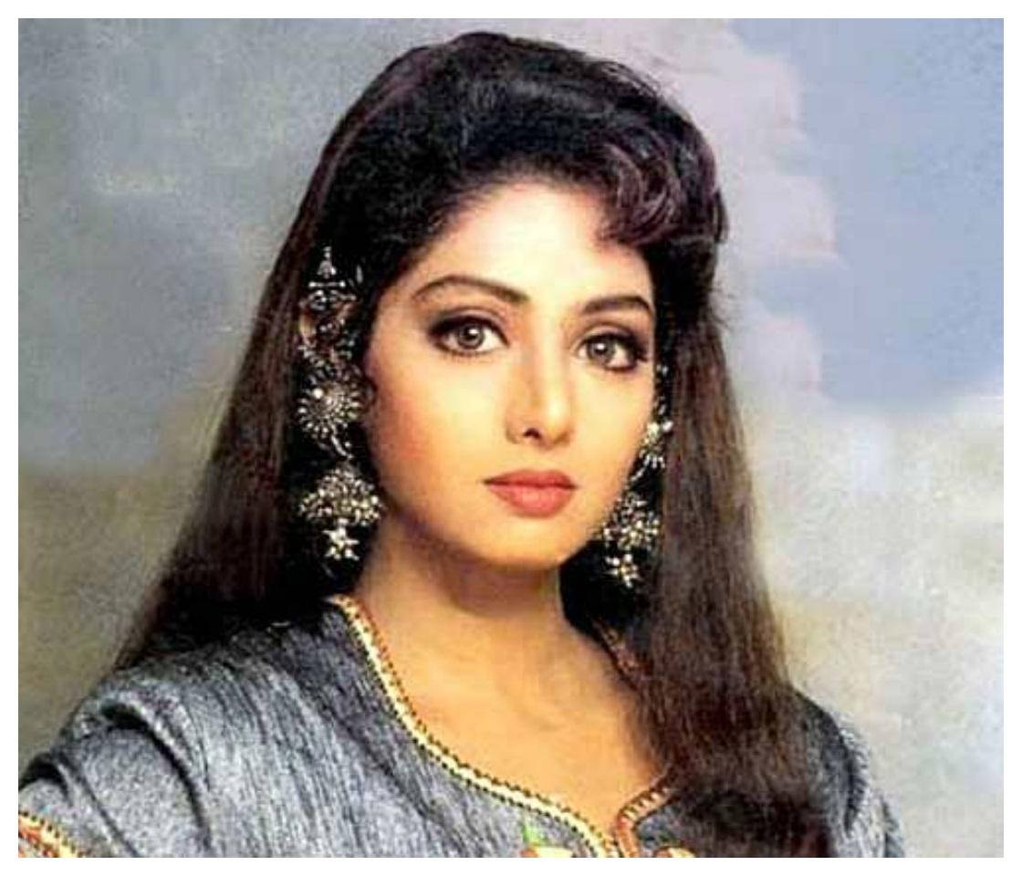 Sridevi 桌布 壁紙 — 一位深色頭髮、戴著華麗耳環的迷人女性，在柔和光線的攝影棚肖像中向前凝視。