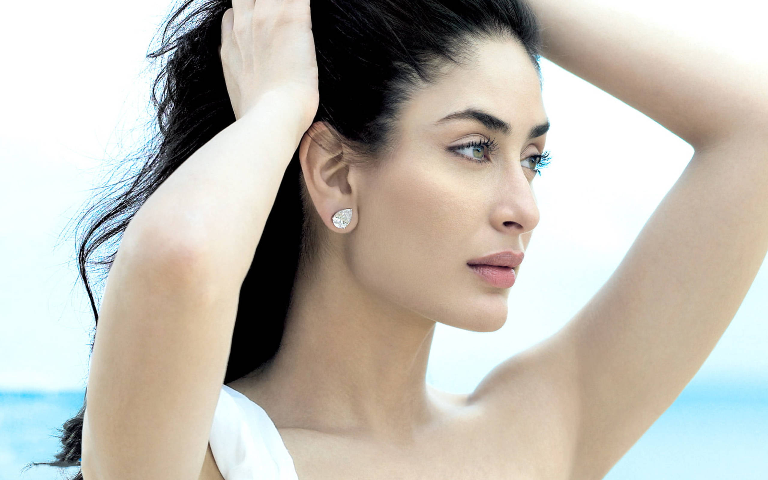 Kareena 桌布 壁紙 — 一位深色頭髮、戴著鑽石耳環的女性，在明亮的藍天和海洋背景下若有所思地凝視著。