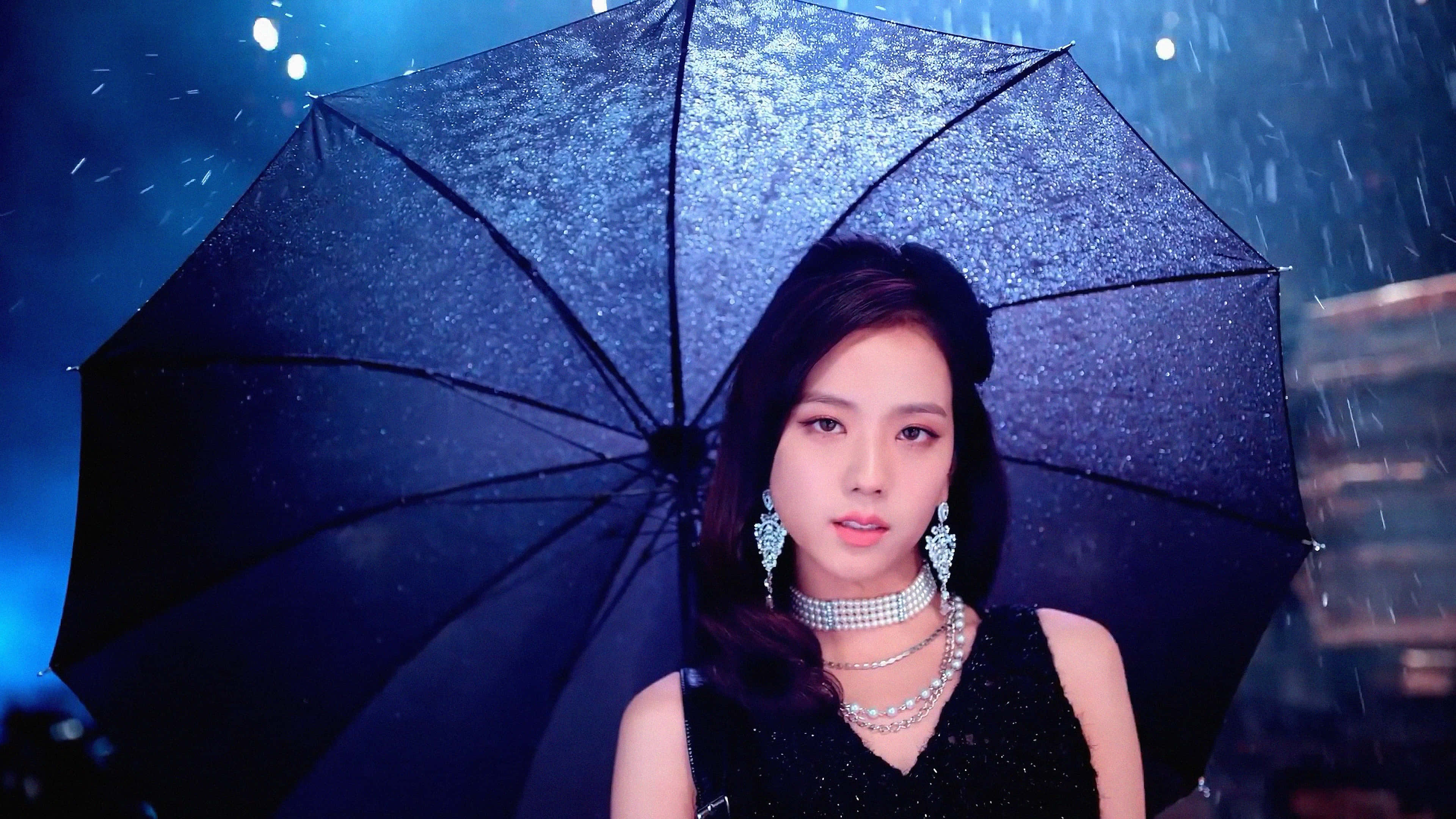 BLACKPINK 桌布 壁紙 — 一位深色頭髮、戴著閃亮珠寶的女性，在藍色背景的雨中撐著一把閃閃發光的黑色雨傘。