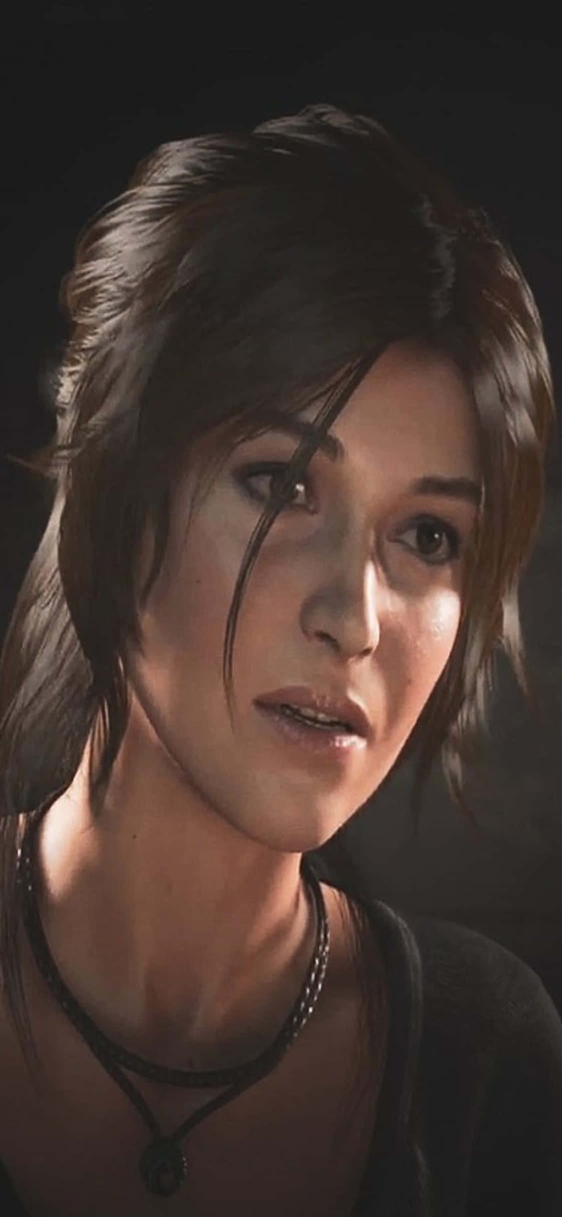 iPhone X Shadow Of The Tomb Raider 桌布 壁紙 — 一位深色頭髮、戴著項鍊的女性特寫，在深色背景下被柔和光線照亮。