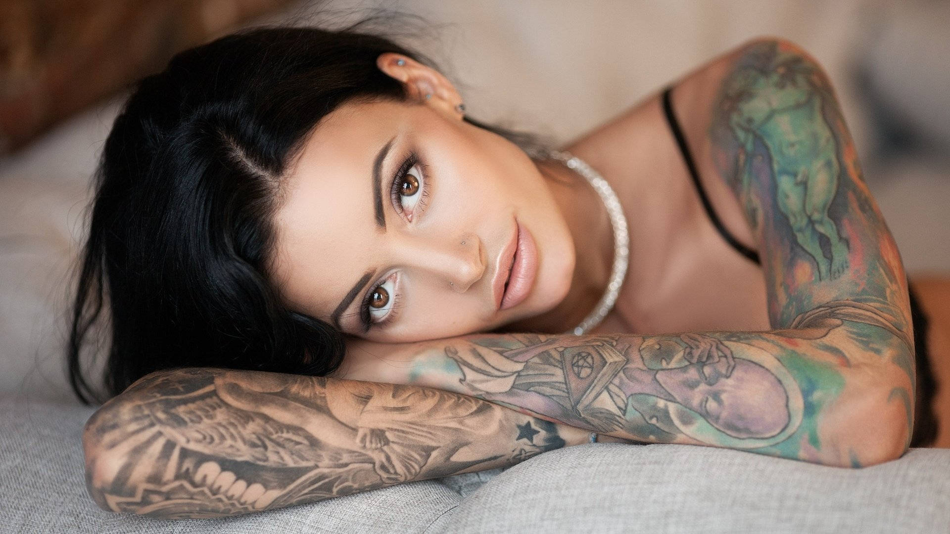 Tattoo 桌布 壁紙 — 一位深色頭髮、擁有複雜彩色刺青的女子，將頭靠在刺青的手臂上，直視鏡頭。