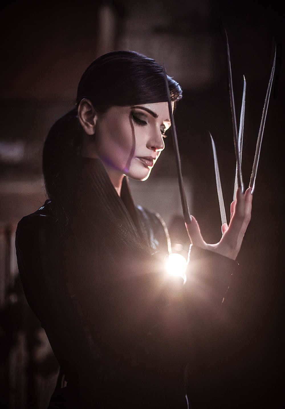 Lady Deathstrike 桌布 壁紙 — 一位深色頭髮、擁有鋒利爪子的女性，在昏暗的環境中將手伸向一道明亮的光。