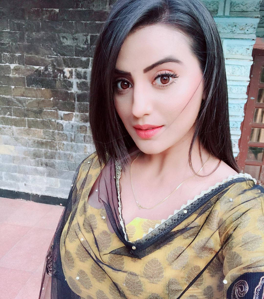 Indian 桌布 壁紙 — 一位深色頭髮、明亮眼睛的女性，穿著圖案黃色上衣，背景是風化的磚牆。
