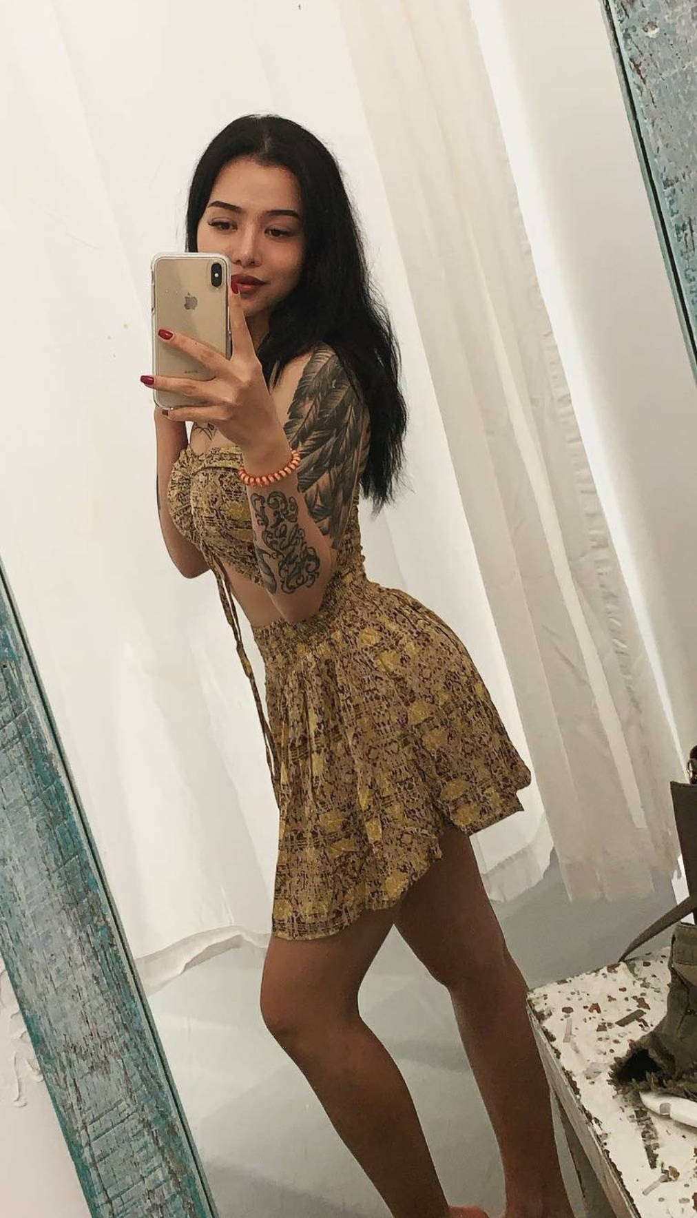 Bella Poarch 桌布 壁紙 — 一位深色頭髮、有刺青的女性，穿著圖案洋裝，在白色窗簾背景下對著鏡子自拍。