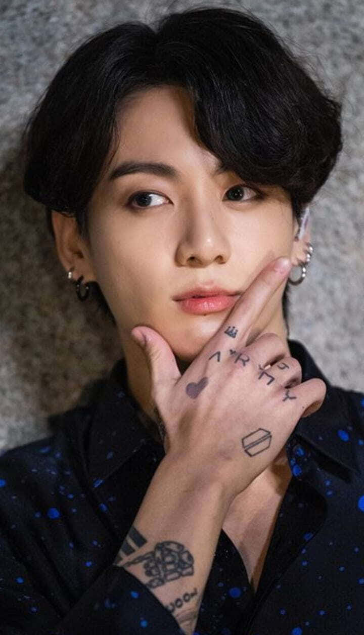 Jungkook 桌布 壁紙 — 一位深色頭髮、有刺青的年輕男子，輕輕將臉貼在紋理灰色牆上。