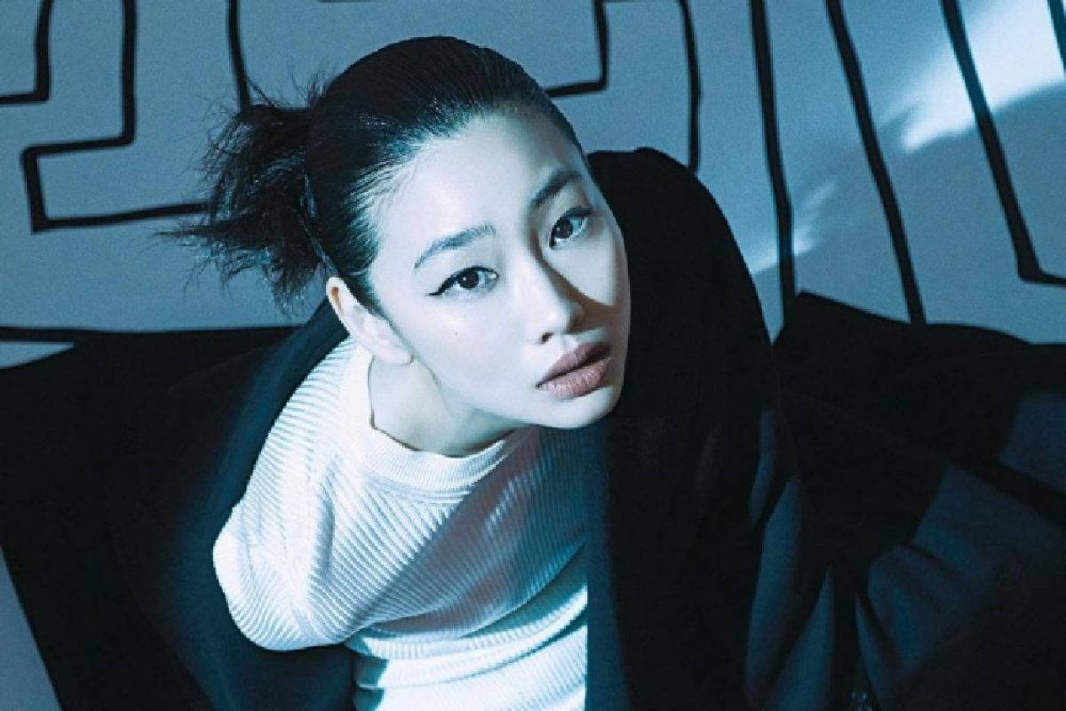 桌布 壁紙 — 一位深色頭髮、梳著凌亂髮髻的女性，在冷藍色燈光下，對著幾何牆壁，凝視著鏡頭。
