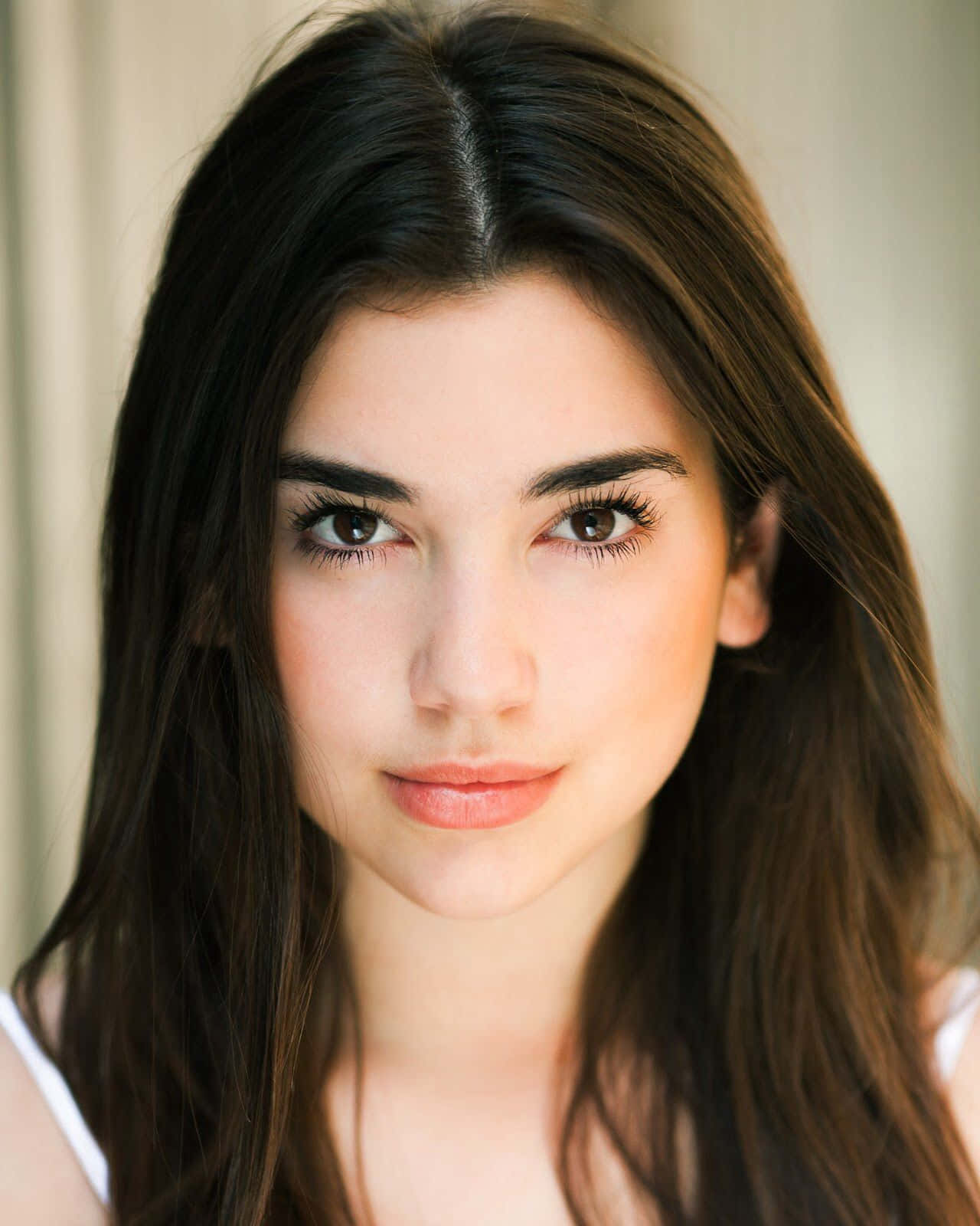 Dua Lipa 桌布 壁紙 — 一位深色頭髮、溫暖棕色眼睛的年輕女性，帶著溫柔的微笑直視鏡頭的近距離肖像。