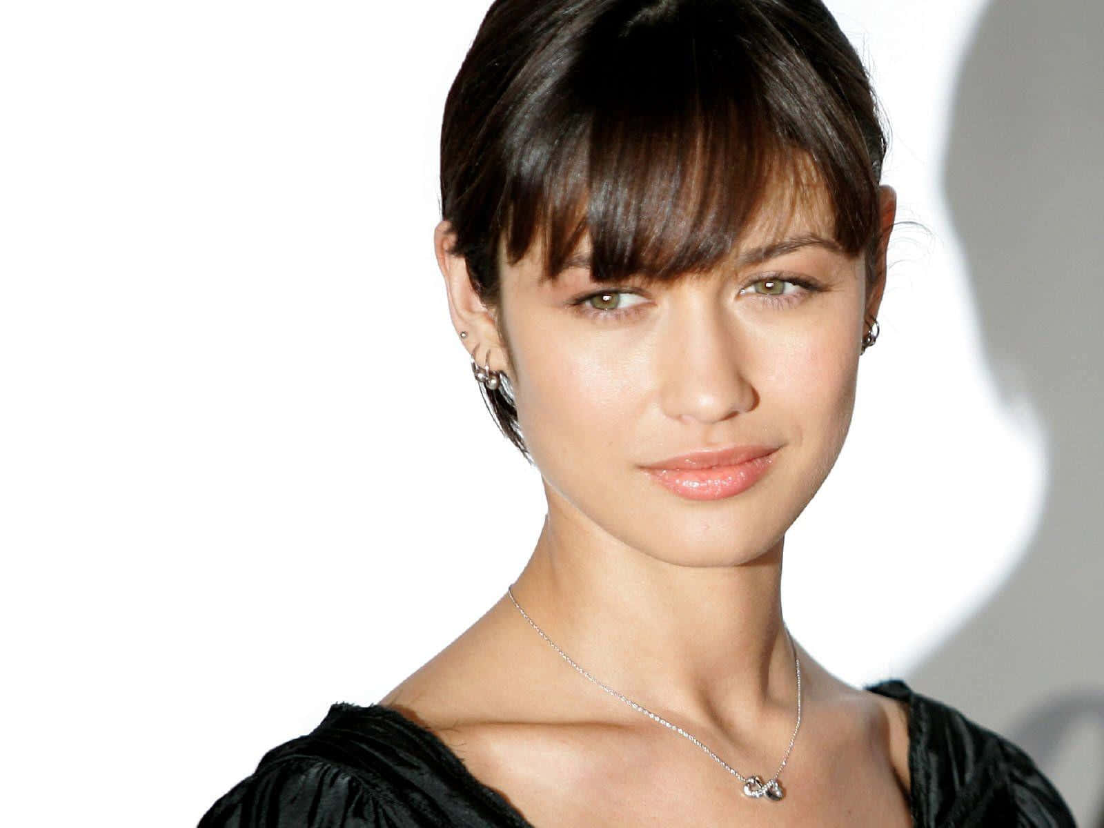 Olga Kurylenko 桌布 壁紙 — 一位深色頭髮、溫柔微笑的女性特寫肖像，背景為明亮的白色。