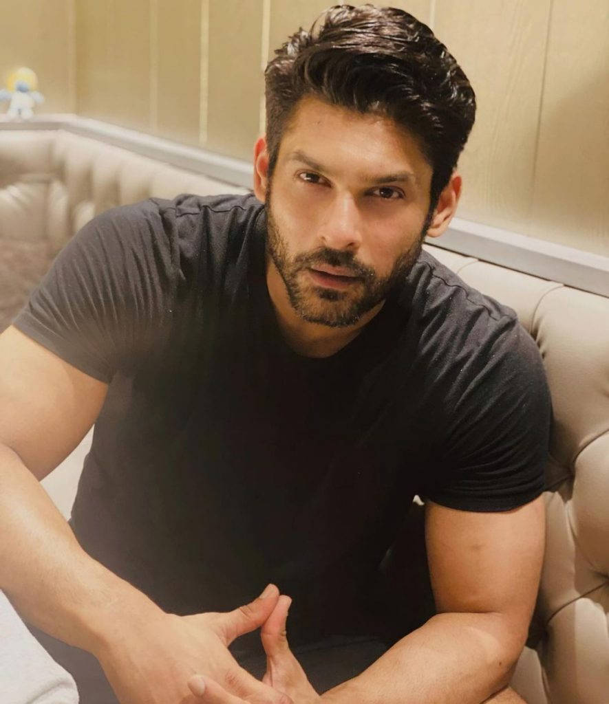 Sidharth Shukla 桌布 壁紙 — 一位深色頭髮、留鬍鬚的男人坐在米色簇絨沙發上，身穿黑色T恤，直視鏡頭。
