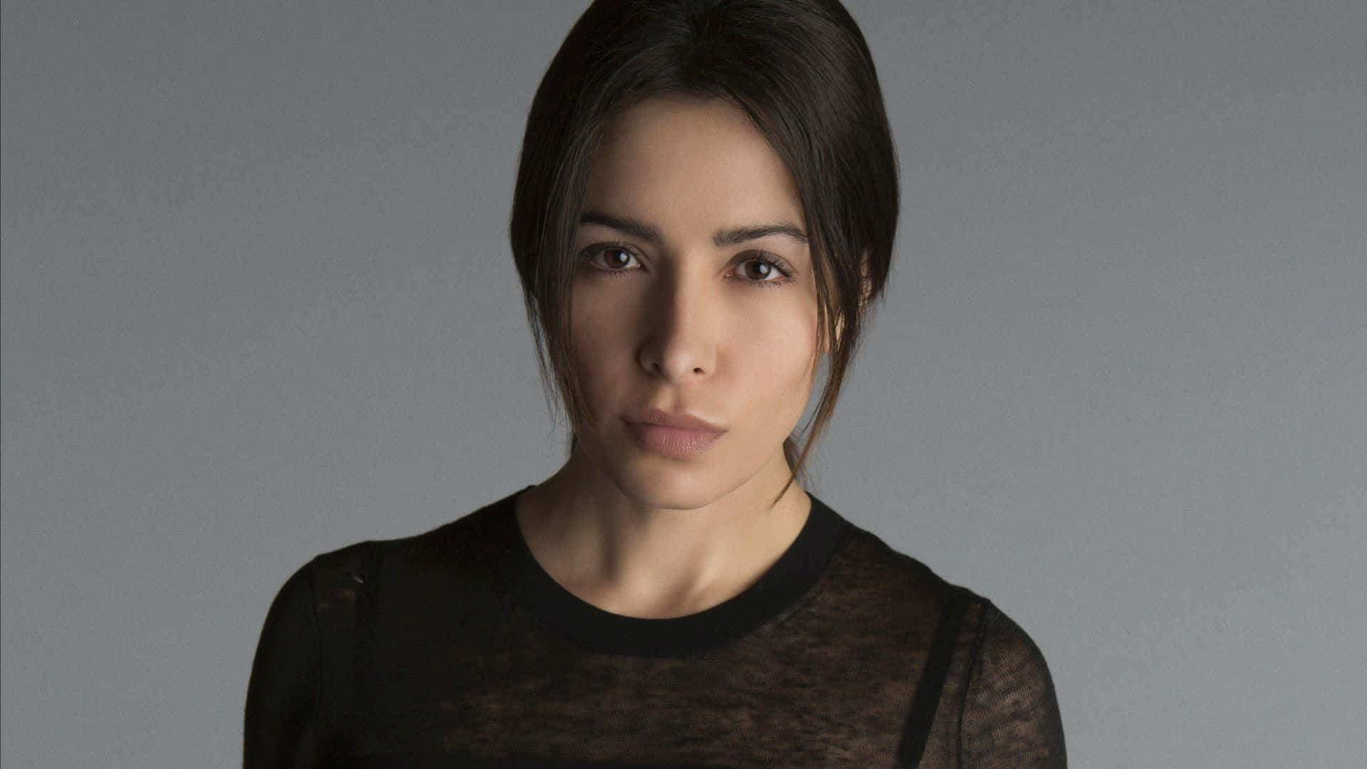 sarah shahi 桌布 壁紙 — 一位深色頭髮、目光強烈的女性在純灰色背景下直視鏡頭。