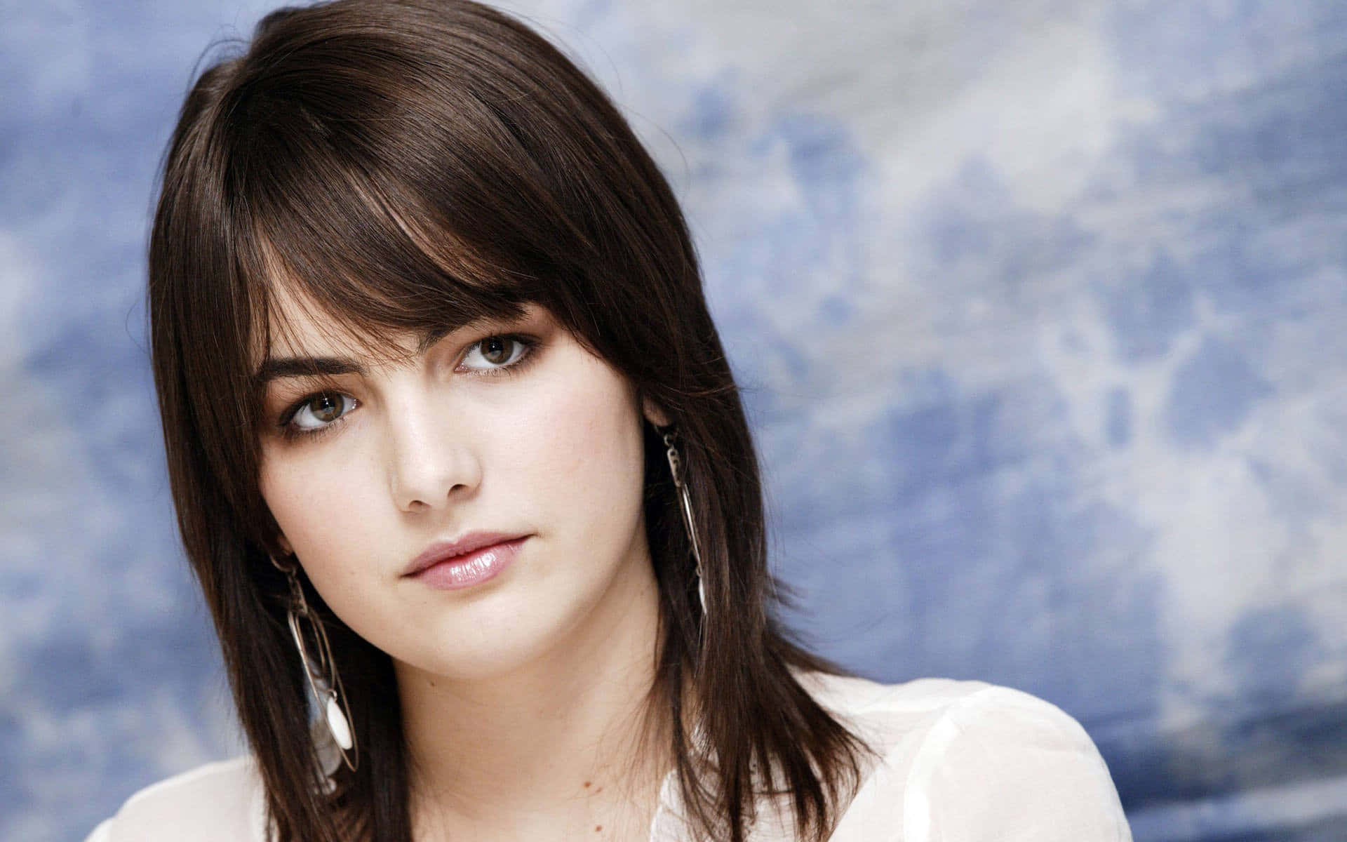Camilla Belle 桌布 壁紙 — 一位深色頭髮、眼睛引人注目的女性的特寫肖像，背景是柔和的藍色紋理。