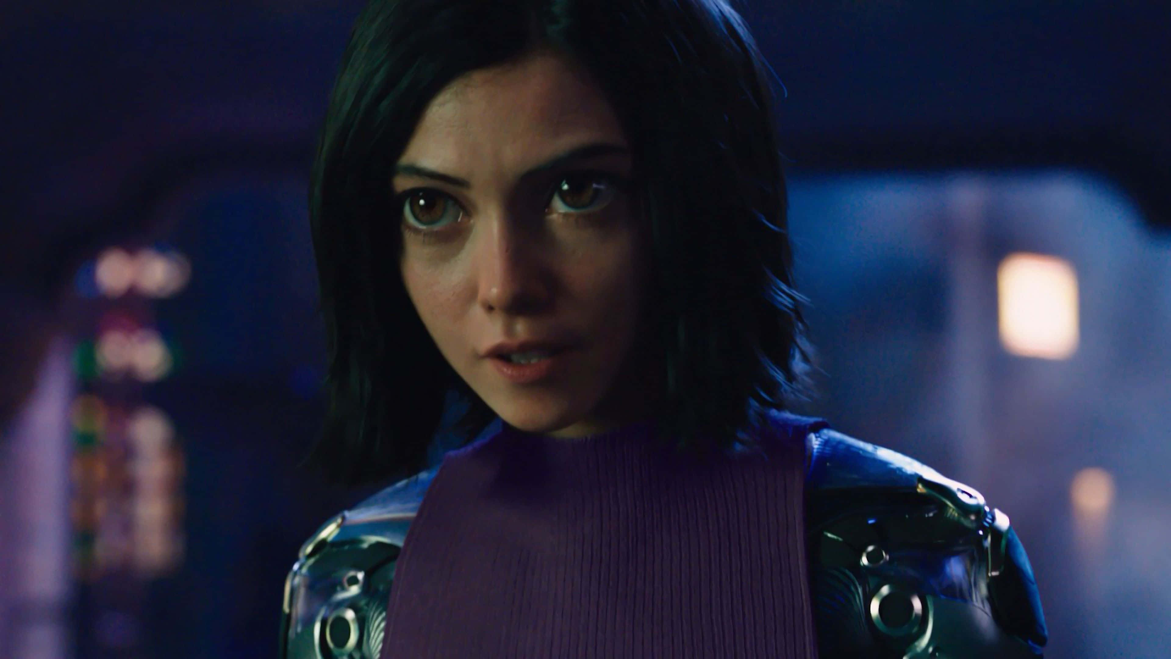 Alita Battle Angel 桌布 壁紙 — 一位深色頭髮、眼睛發光的賽博龐克女性在昏暗的未來場景中專注地凝視。
