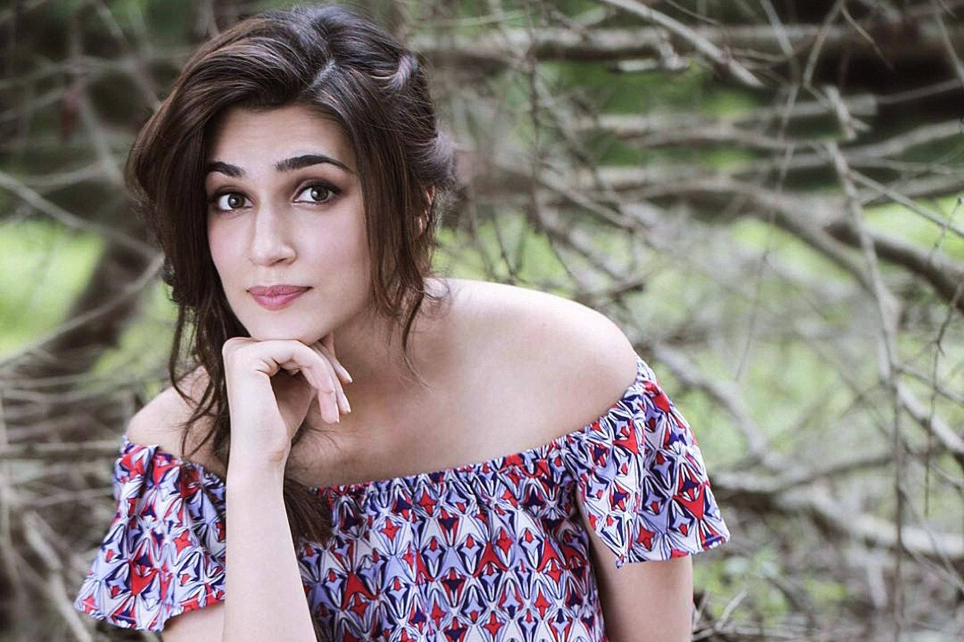 Kriti 桌布 壁紙 — 一位深色頭髮、穿著圖案露肩上衣的女性，在模糊的自然背景下將下巴靠在手上。