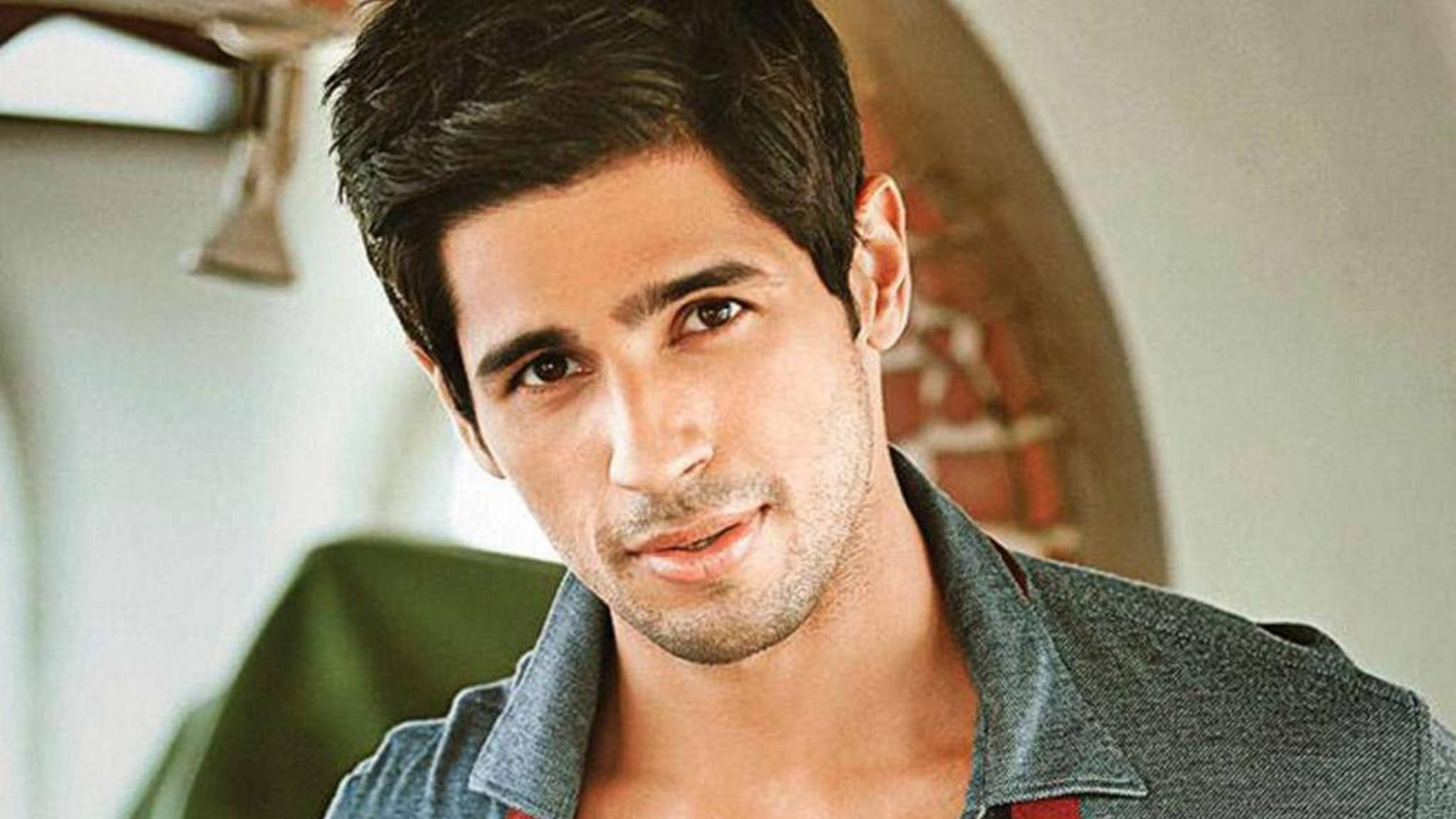 Sidharth Malhotra 桌布 壁紙 — 一位深色頭髮、穿著牛仔襯衫、帶著含蓄微笑的英俊男士的特寫肖像。