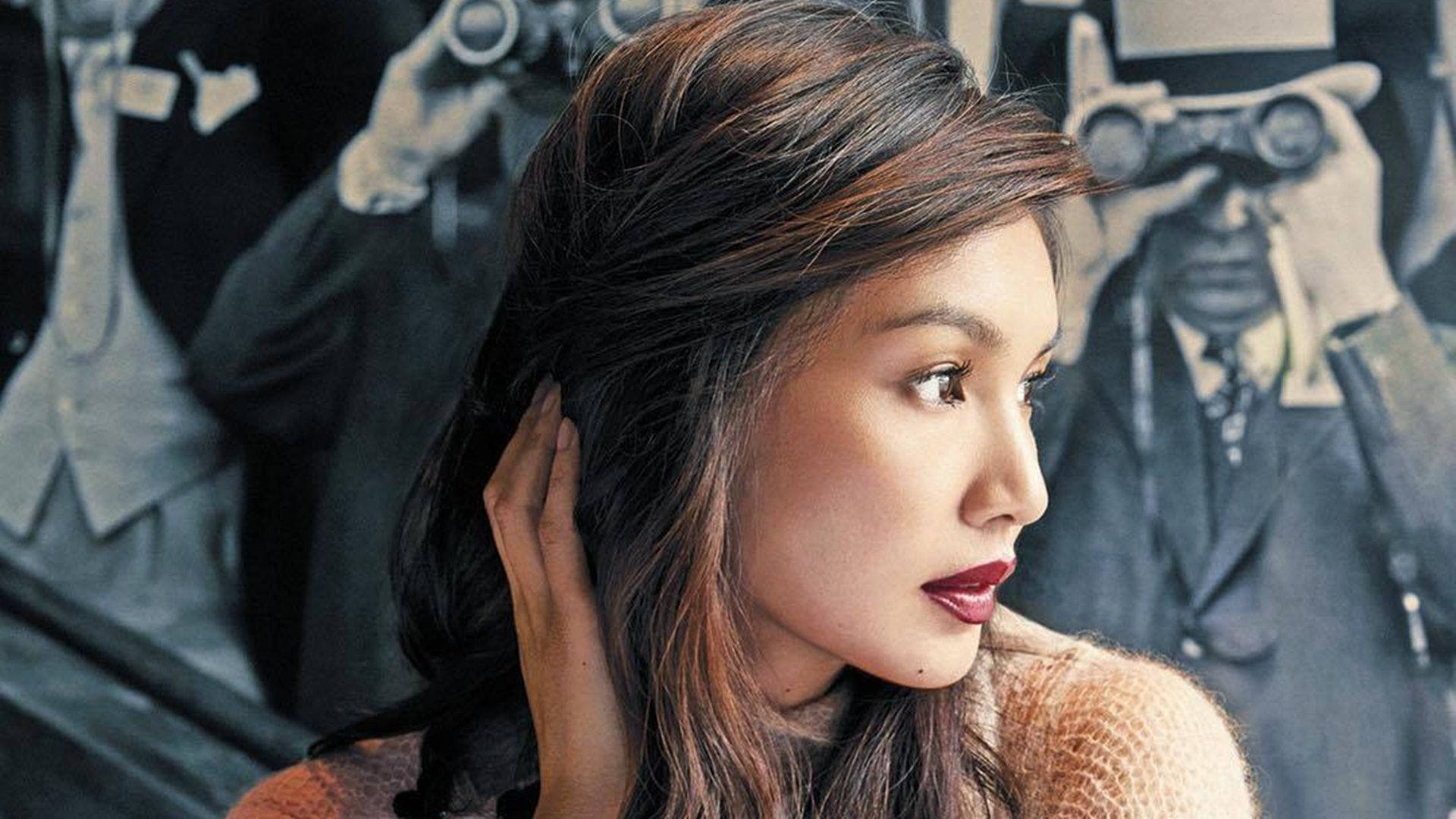 Gemma Chan 桌布 壁紙 — 一位深色頭髮、紅唇的女性若有所思地凝視著，而攝影師們用復古相機在充滿氛圍的攝影棚中捕捉她的身影。