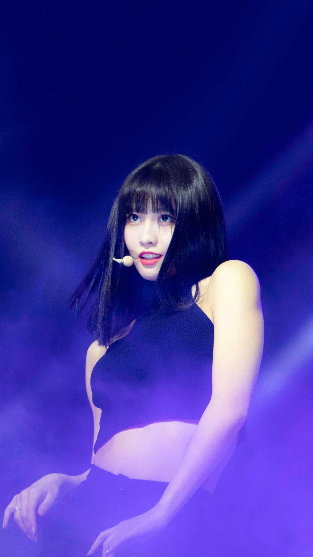 Momo 桌布 壁紙 — 一位深色頭髮、紅唇的女性表演者在充滿煙霧效果的鮮豔紫色舞台燈光下自信地擺姿勢。