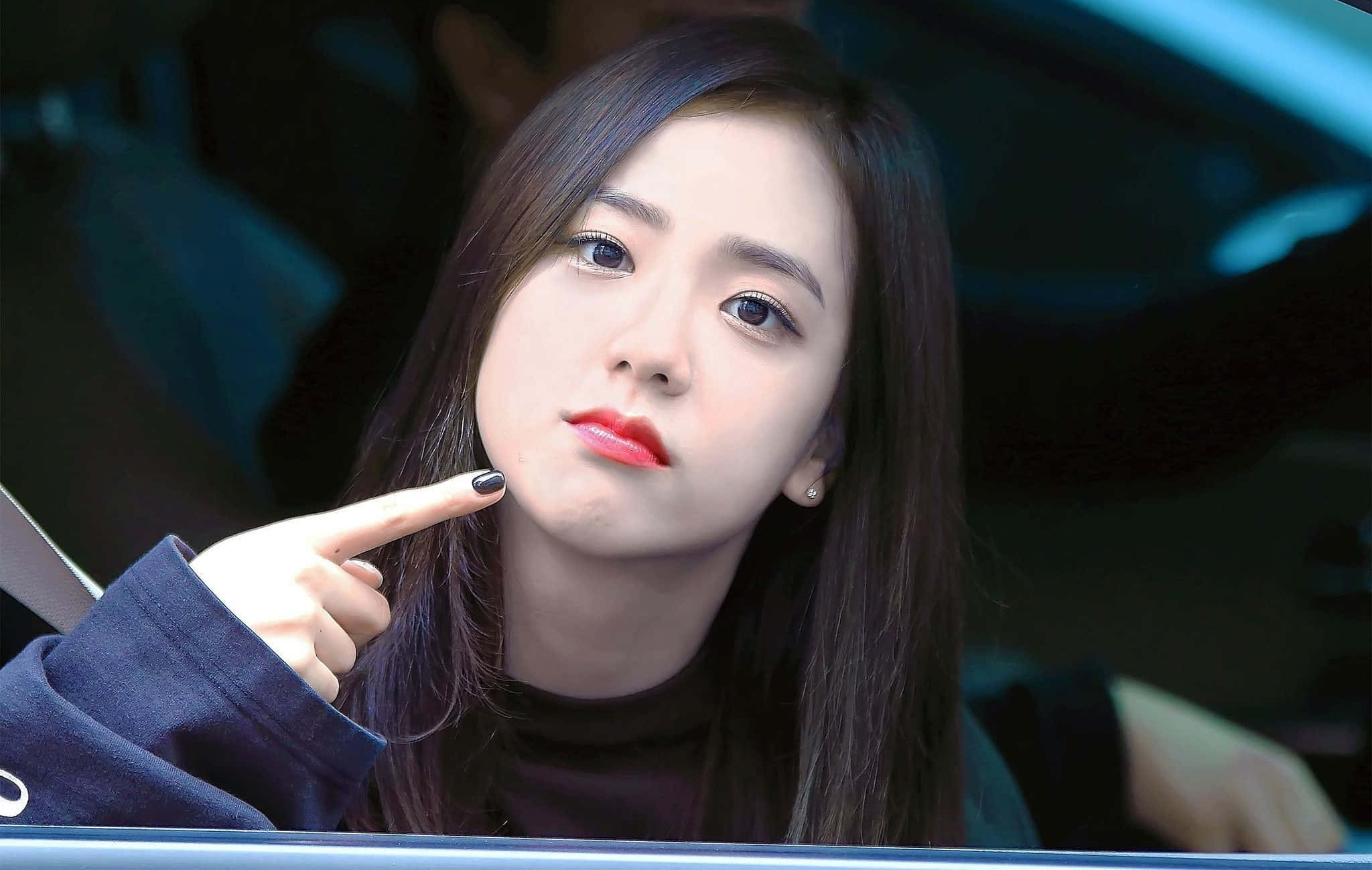 BLACKPINK 桌布 壁紙 — 一位深色頭髮、紅唇的年輕女子晚上坐在車內，指著自己的臉頰。