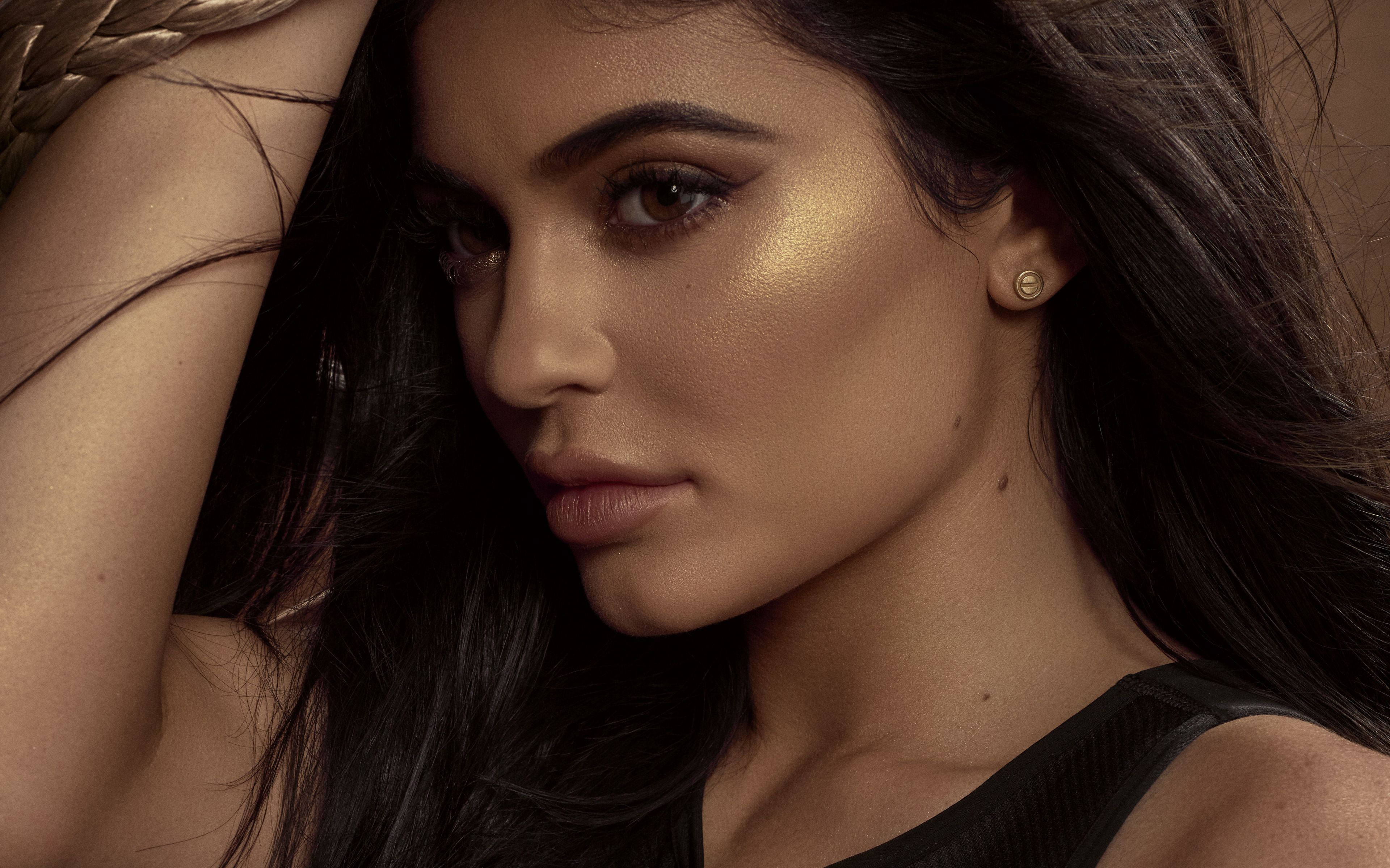 Kylie 桌布 壁紙 — 一位深色頭髮、臉頰帶有金色打亮的迷人女性，溫柔地凝視著鏡頭。