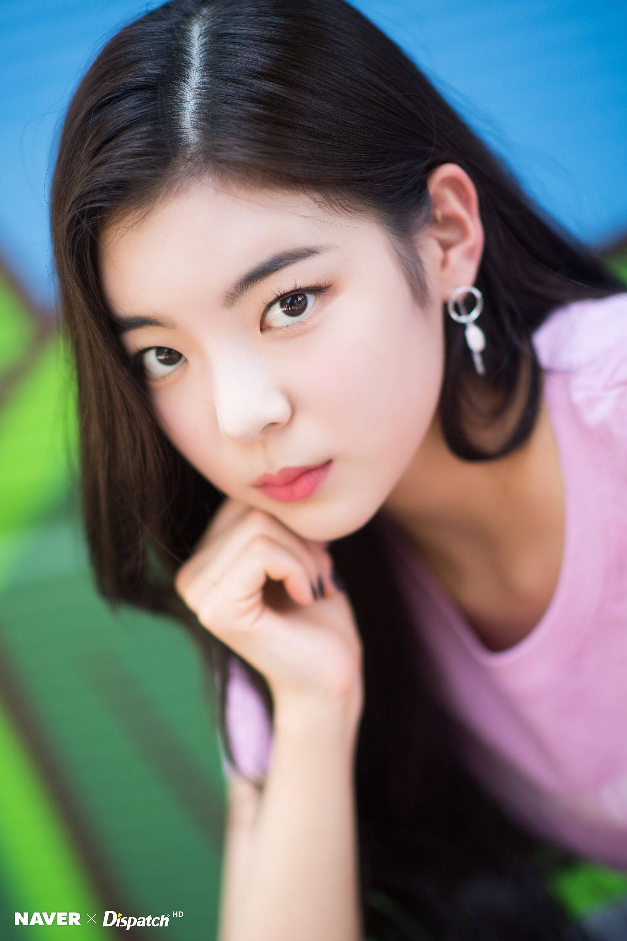 Lia 桌布 壁紙 — 一位深色頭髮、身穿粉紅色上衣的年輕女性，在充滿活力的藍色和綠色模糊背景前，將下巴靠在手上，直視鏡頭。