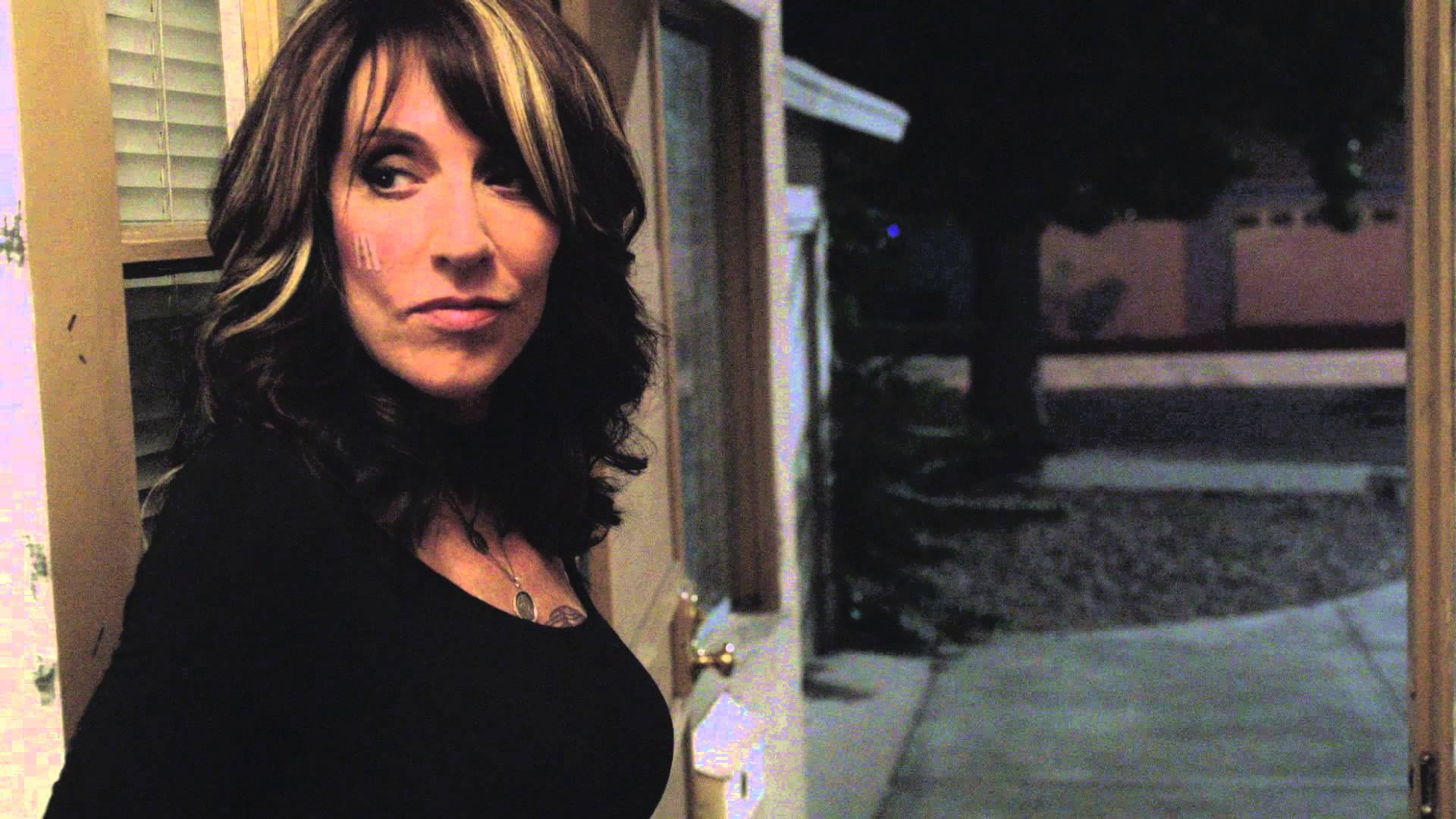 電影動圖 桌布 壁紙 — 一位深色頭髮、身穿黑色上衣的女性在夜晚站在門口，直視鏡頭，表情嚴肅。