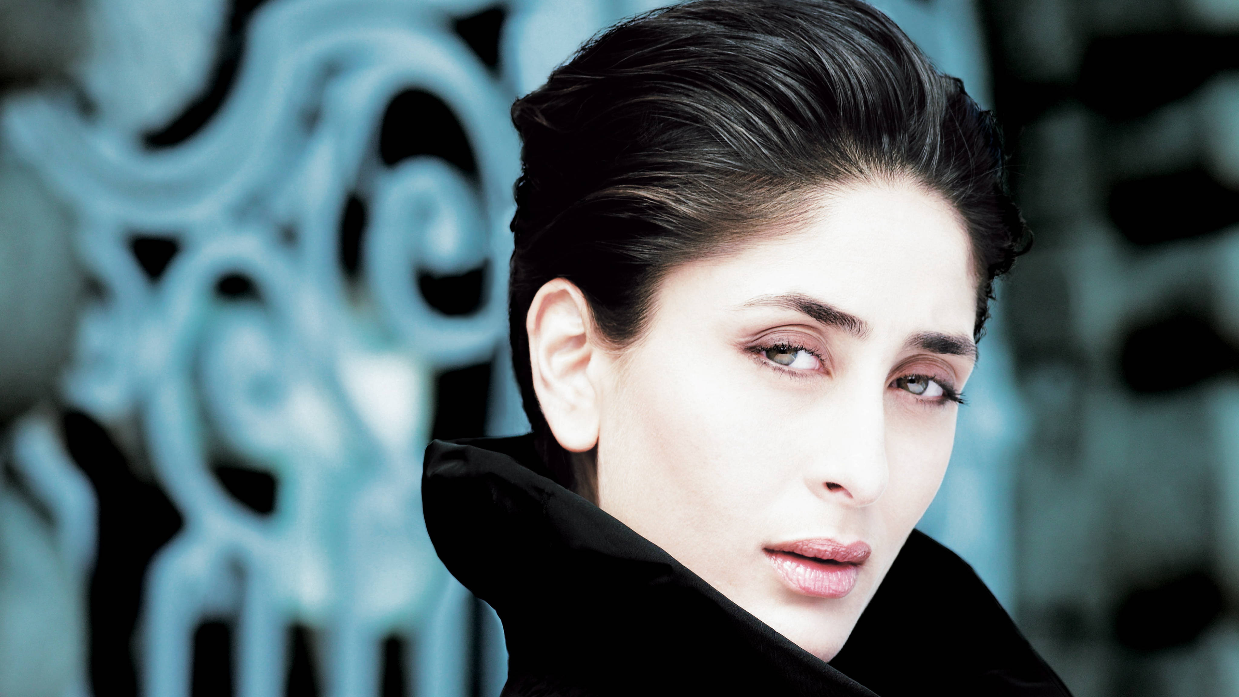Kareena 桌布 壁紙 — 一位深色頭髮、身穿黑色外套的女性，在模糊的華麗藍色和黑色背景前專注地凝視。
