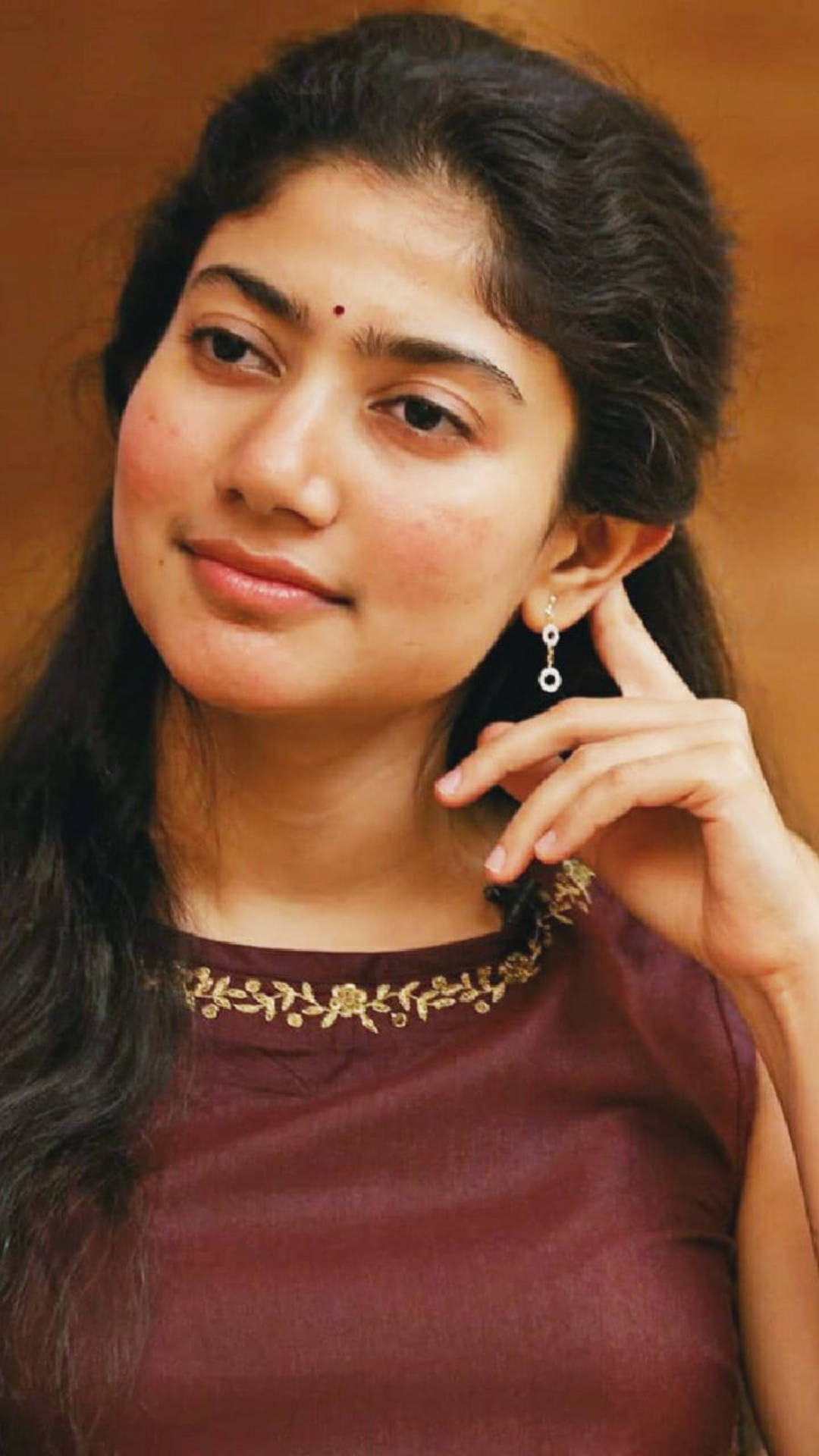 Sai Pallavi 桌布 壁紙 — 一位深色頭髮、額頭上有吉祥痣的女性，輕輕微笑，同時用精緻的耳環觸碰耳朵。