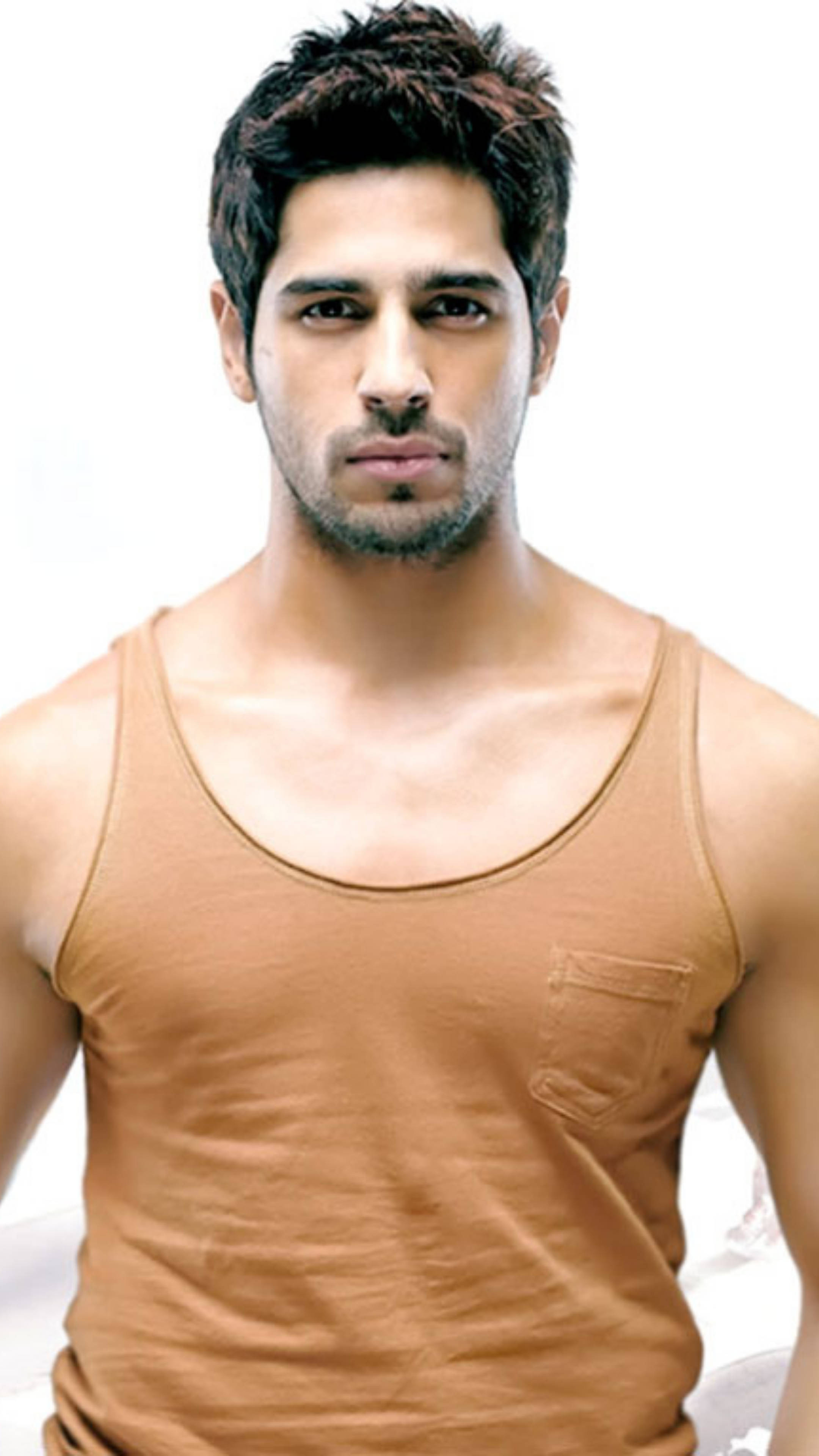 Sidharth Malhotra 桌布 壁紙 — 一位深色頭髮、鬍渣的俊男，身穿米色背心，背景為純白色。