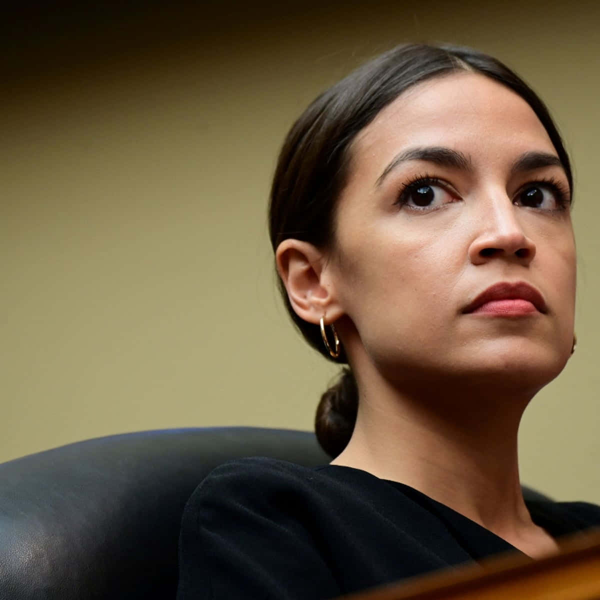 Politics 桌布 壁紙 — 一位深色頭髮向後梳起的女性坐在黑色椅子上，向上看，表情嚴肅。