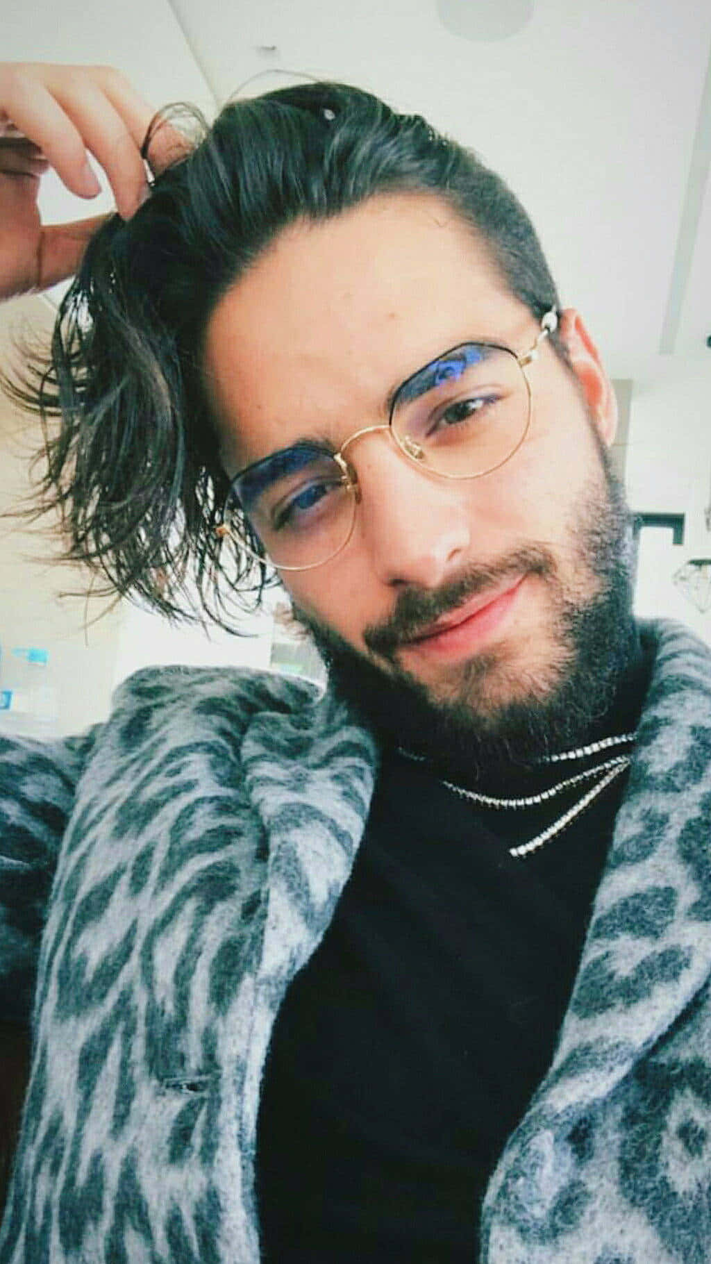 selfie 桌布 壁紙 — 一位深色頭髮和鬍鬚的男子，戴著圓形眼鏡和豹紋外套，在室內整理頭髮。