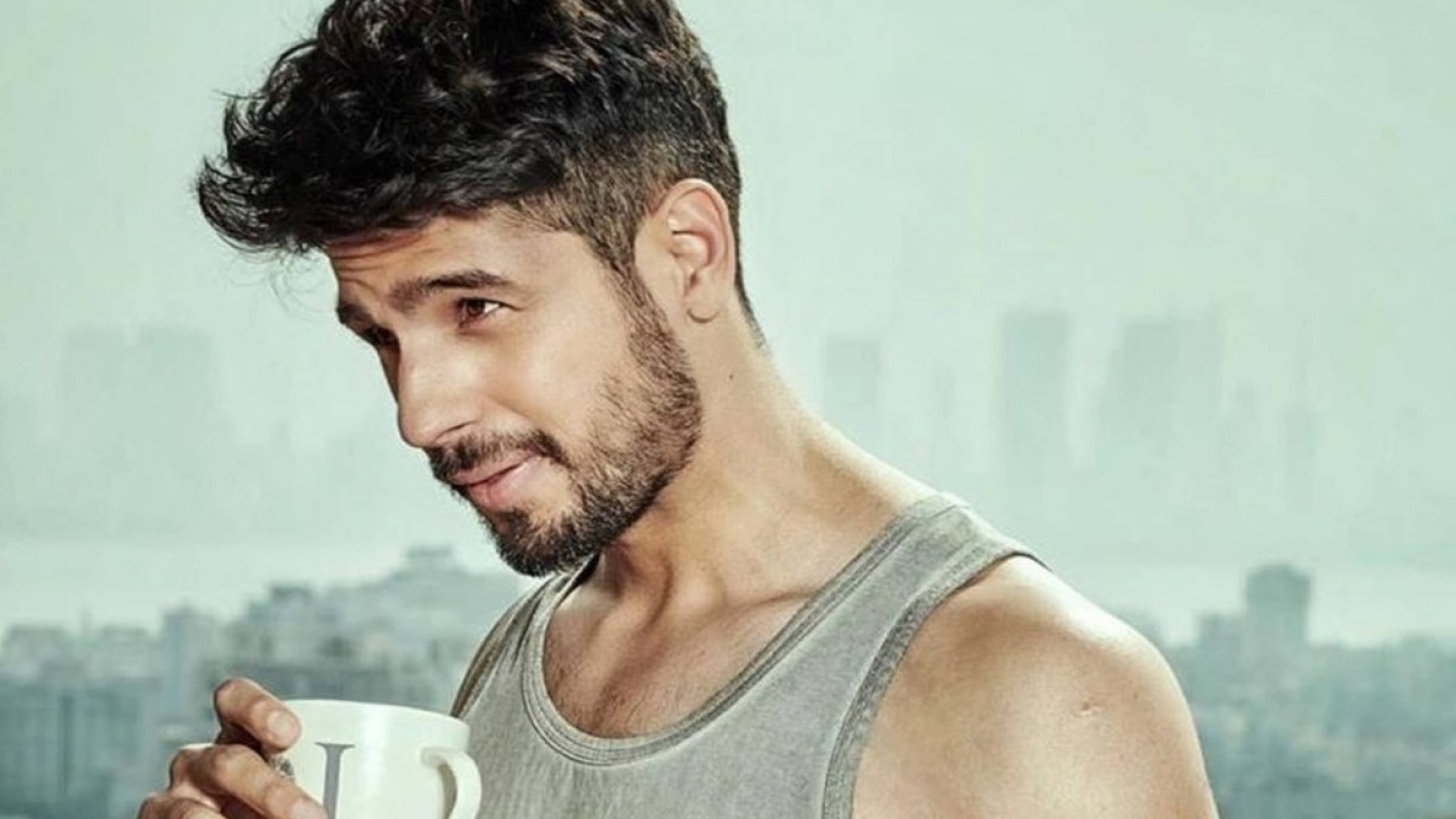 Sidharth Malhotra 桌布 壁紙 — 一位深色頭髮和鬍鬚的英俊男子在模糊的城市天際線背景下啜飲咖啡。