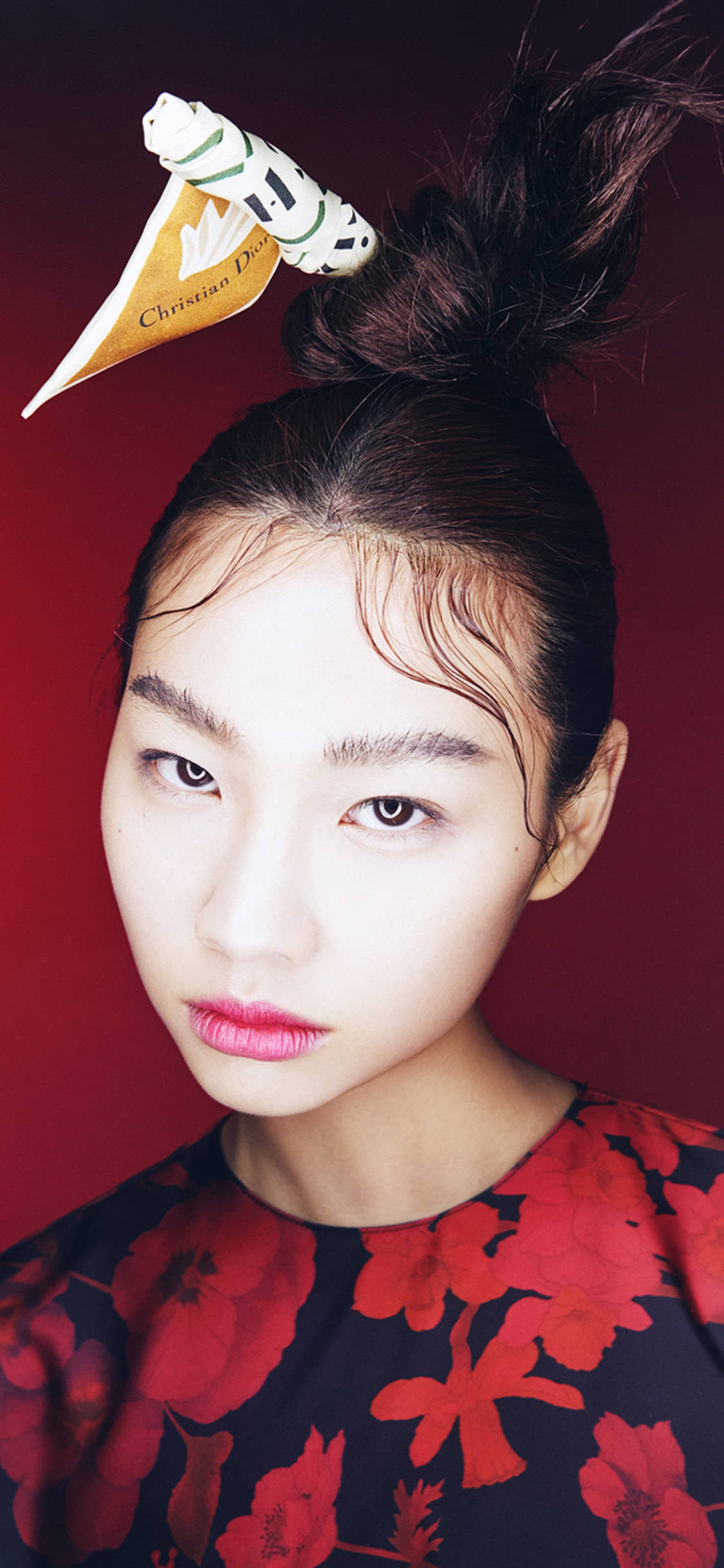 Hoyeon 桌布 壁紙 — 一位深色頭髮束成高髻的女性，在深紅色背景前佩戴Christian Dior帽針和紅色花卉上衣。